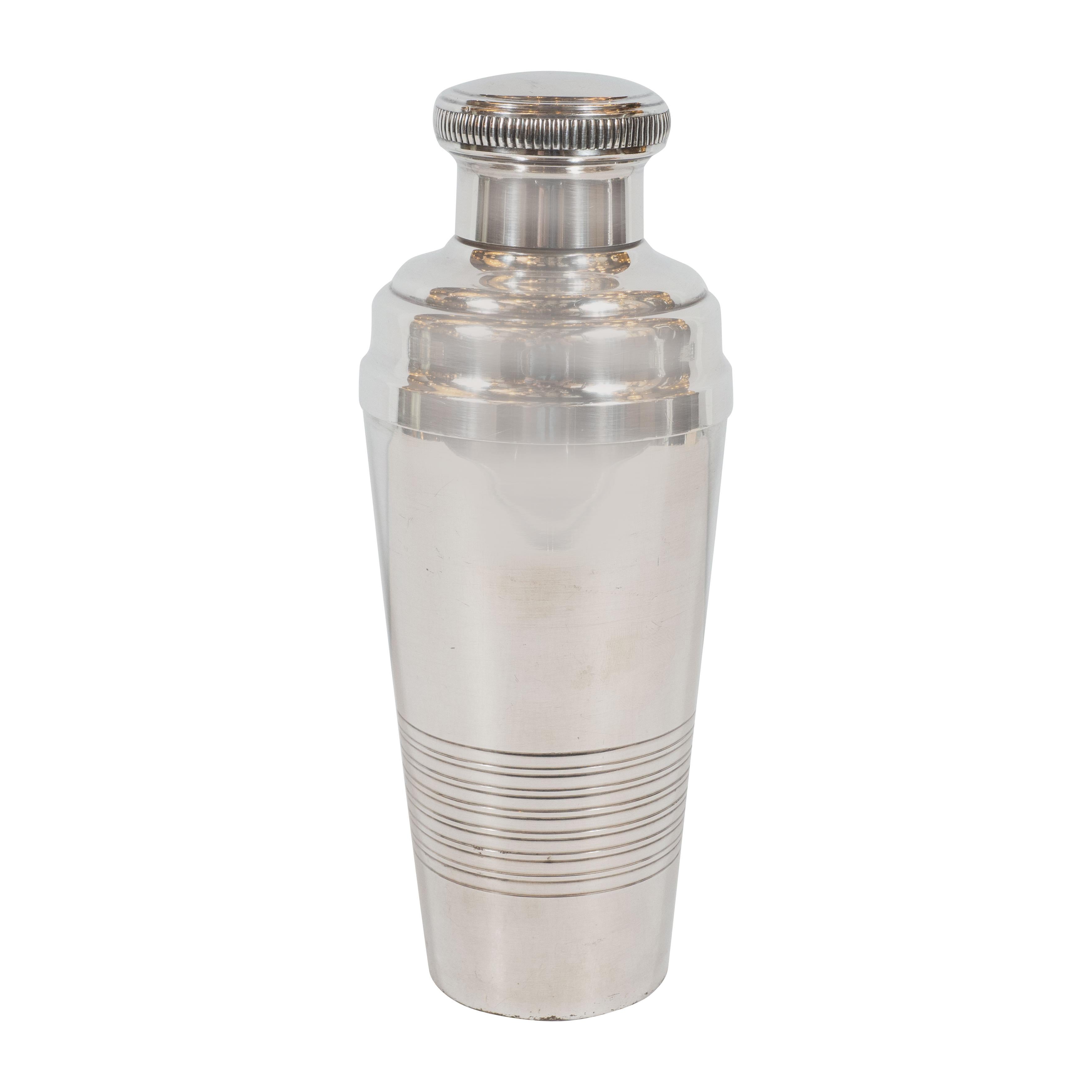This three-piece French Art Deco silver plate cocktail Shaker was realized in France circa 1930. Recalling the sleek machine age aesthetic of late Art Deco, the Shaker's tumbler has a smooth streamlined profile, which is circumscribed by a pattern