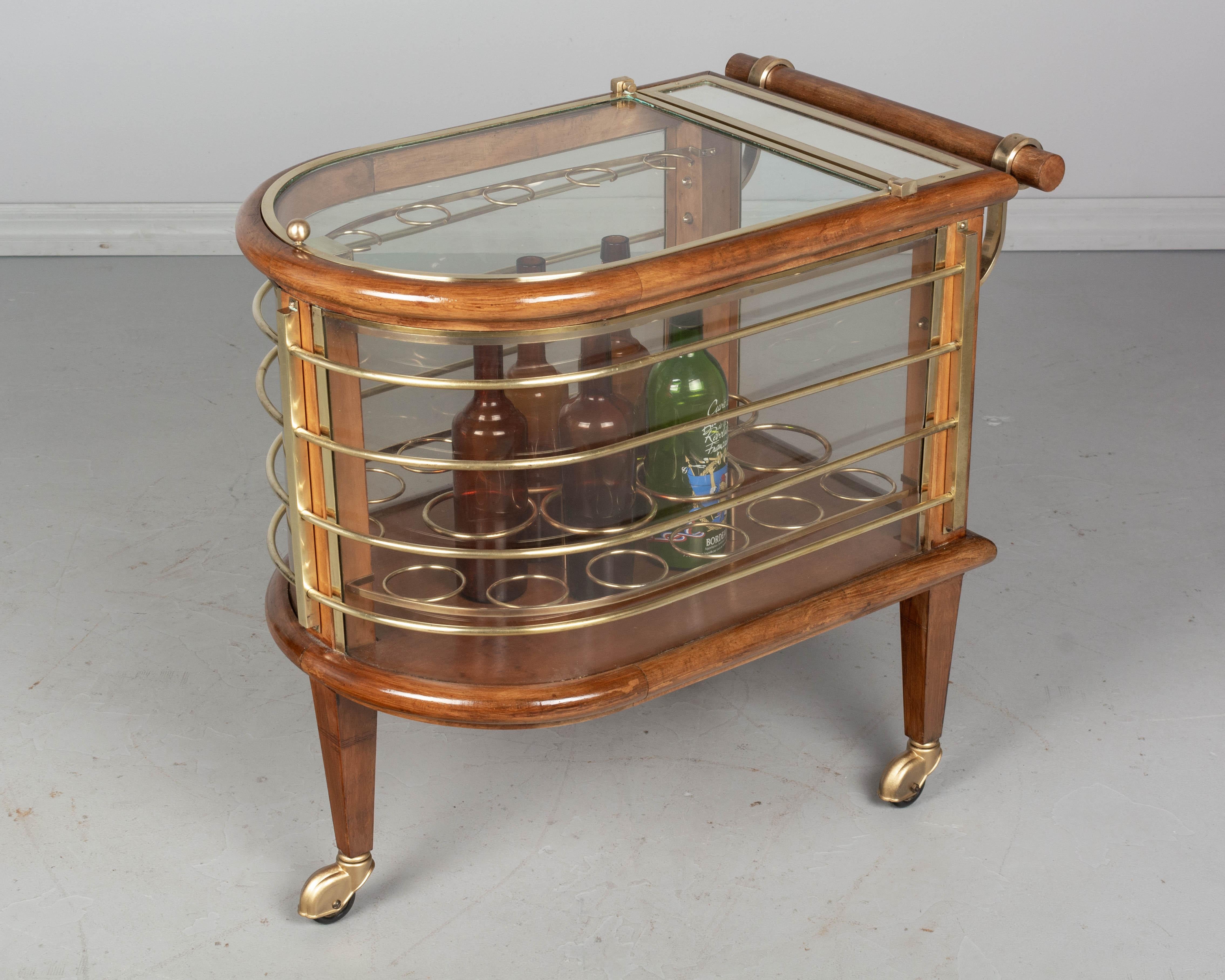 A Mid-Century Modern French Art Deco style bar cart designed by Louis Sognot. Classic ocean liner styling including a rounded end with brass wire railings, simulating a ship deck. Made of solid beechwood with curved plexiglass sides and a hinged,