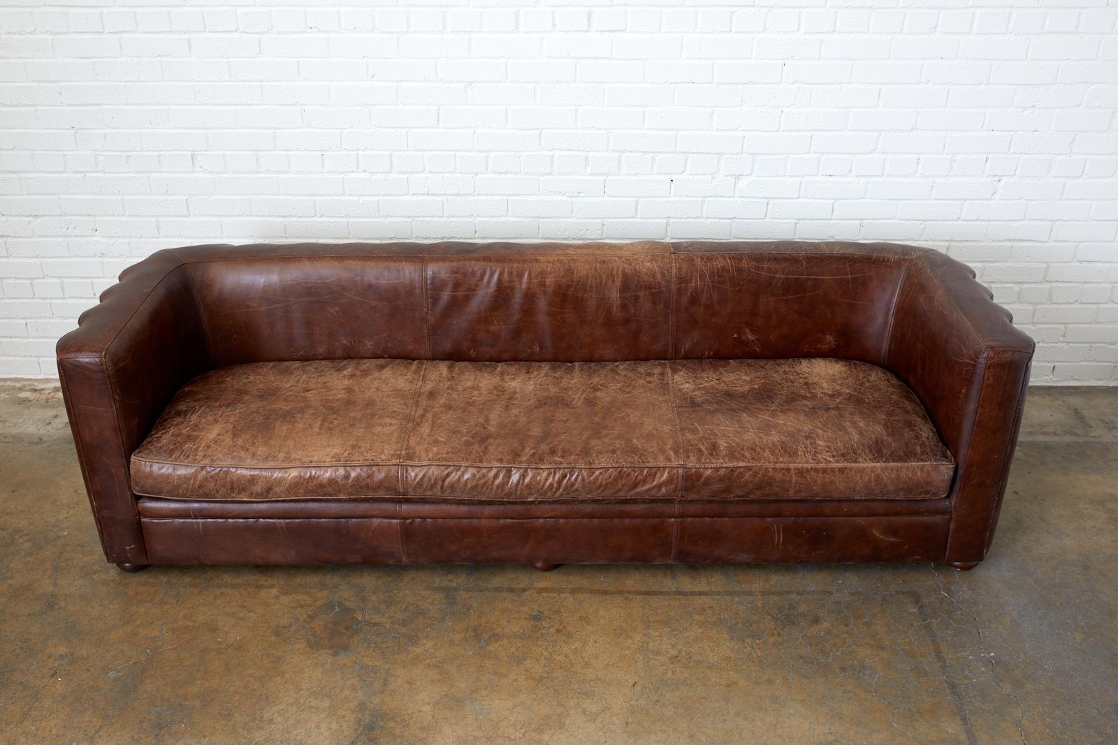 Dramatic French Art Deco style sofa featuring a low slung tuxedo design frame with a padded channel back bordered by brass tack nailheads. Made with vintage cigar leather having a beautiful aged patina. Excellent joinery and craftsmanship with a