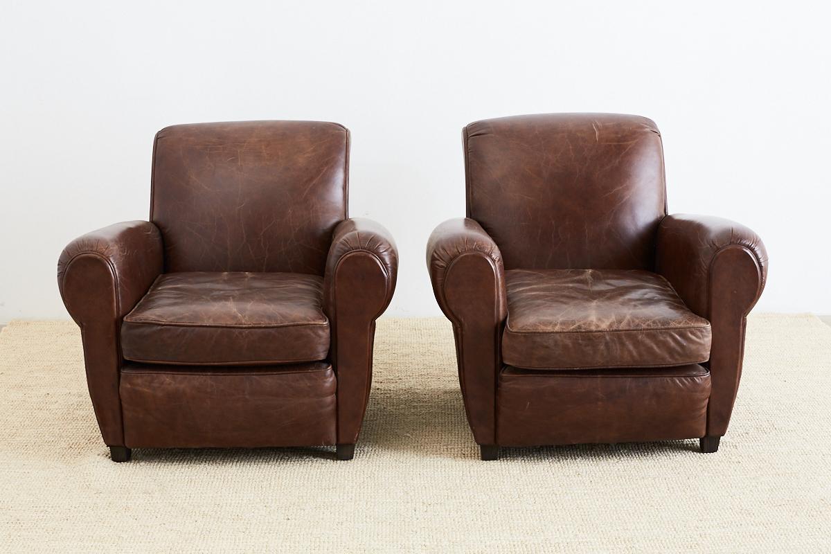 Classic pair of French Art Deco style cigar leather club chairs featuring a beautiful distressed leather patina. Made from thick top grain English leather hides finished in Italy. The backs are bordered with dark brass tack nailhead trim.