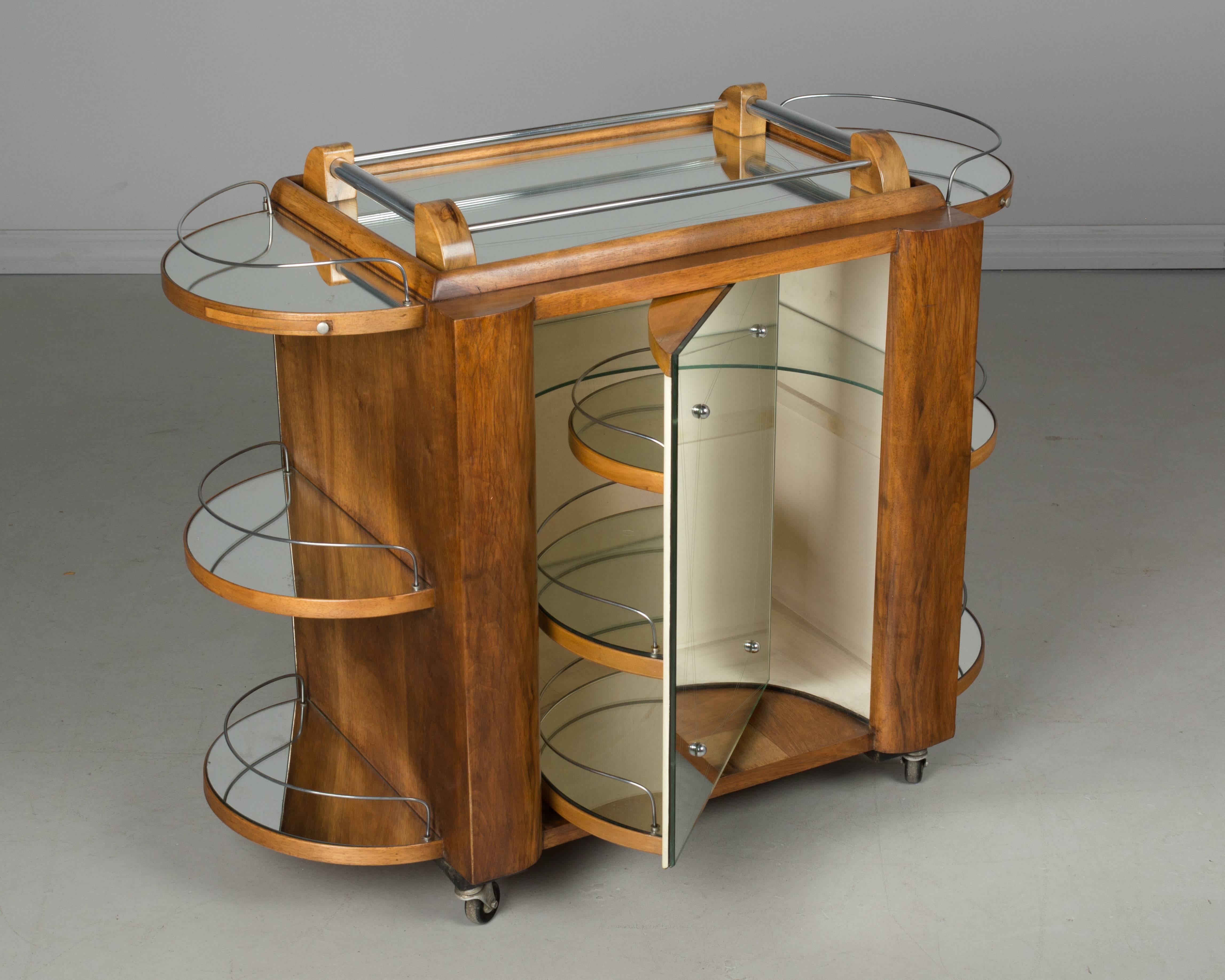 A French Art Deco style mirrored rolling bar cabinet by Bar Tugas made of veneer of walnut. Classic ocean liner styling includes rounded ends with metal wire railings, simulating a ships deck. The etched mirror front door swings open to reveal
