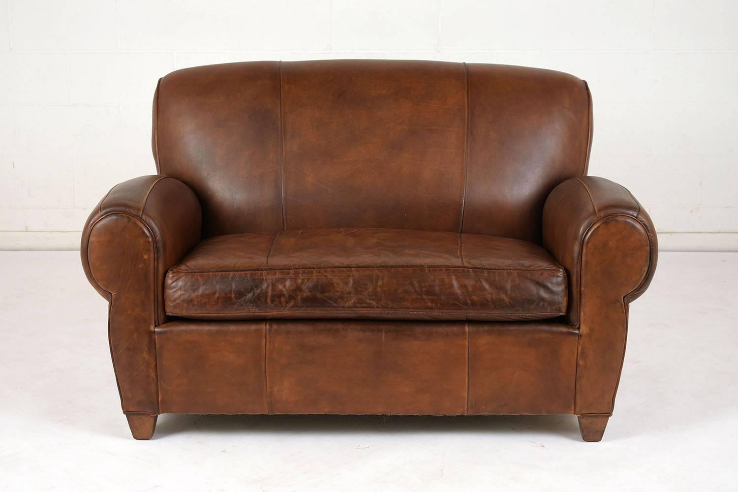 This 1970s French Art Deco-style loveseat is upholstered in a brown color leather with a naturally distressed finish and single piping trim details throughout. The very comfortable 5 inch thick cushion extends the entire length of the loveseat. The