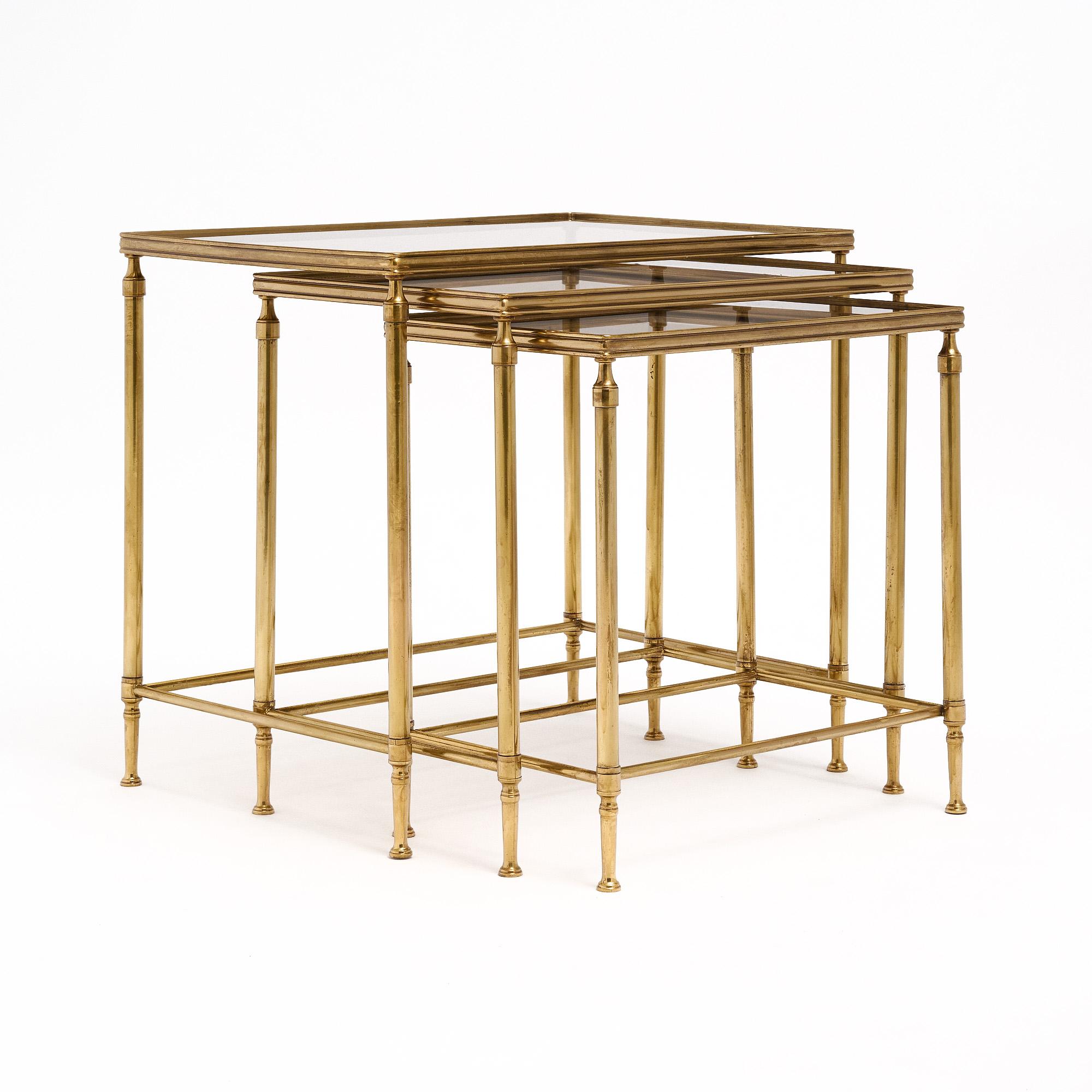 Set of three nesting tables from France with brass structures and smoked glass tops. Each of the original glass tops features a mirrored edge.

Large Table: 
Height - 20”
Length - 22.25”
Depth - 16”

Medium Table: 
Height - 18.75”
Length - 20”
Depth