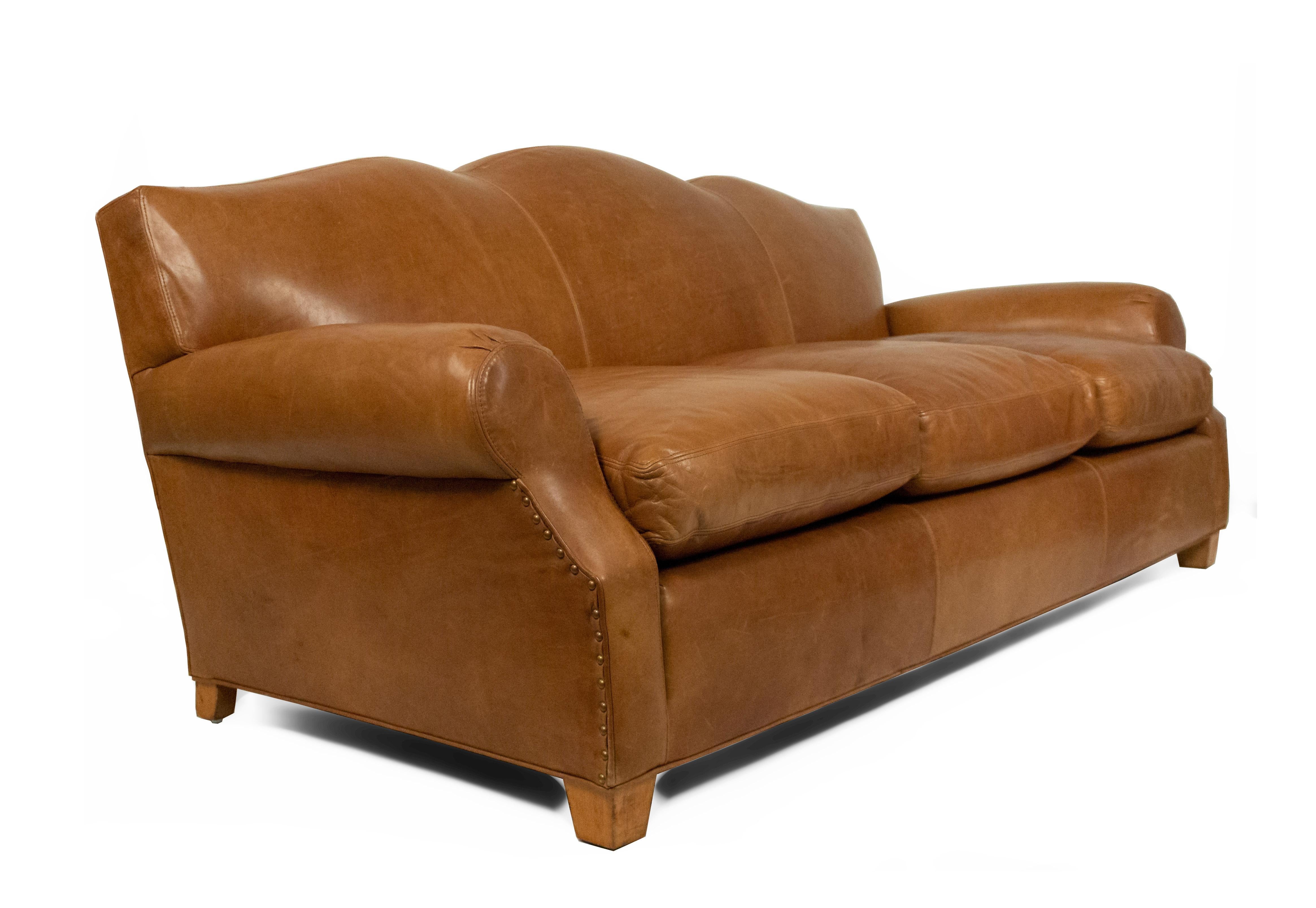 French Art Deco style tan leather camel back sofa with scrolled arms and three-seat cushion on wooden block feet.