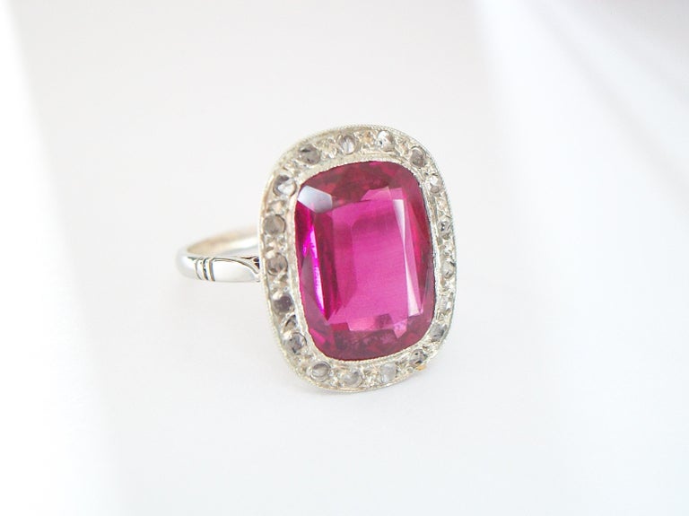 French Art Deco Synthetic Ruby and Diamond halo ring - featuring a milgrain set Emerald cut lab grown Ruby (approx. 3.79 carats - 12 x 9 x 4 mm.) - surrounded by 18 round prong set old cut diamonds (each a little over 1 mm. in diameter) - 18 Karat