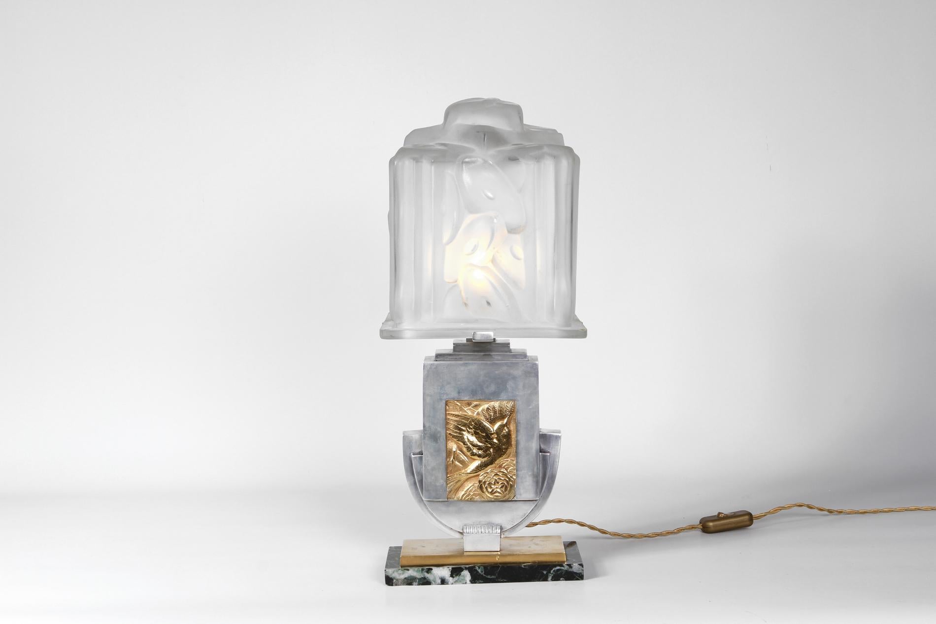 French Art Deco table lamp by Degué from 1930. Special model with base in marble, bronze in silver and gold and big glass lampshade. In the middle there is the decor of a bird with a flower in all gold details. 
The piece has a real impact and