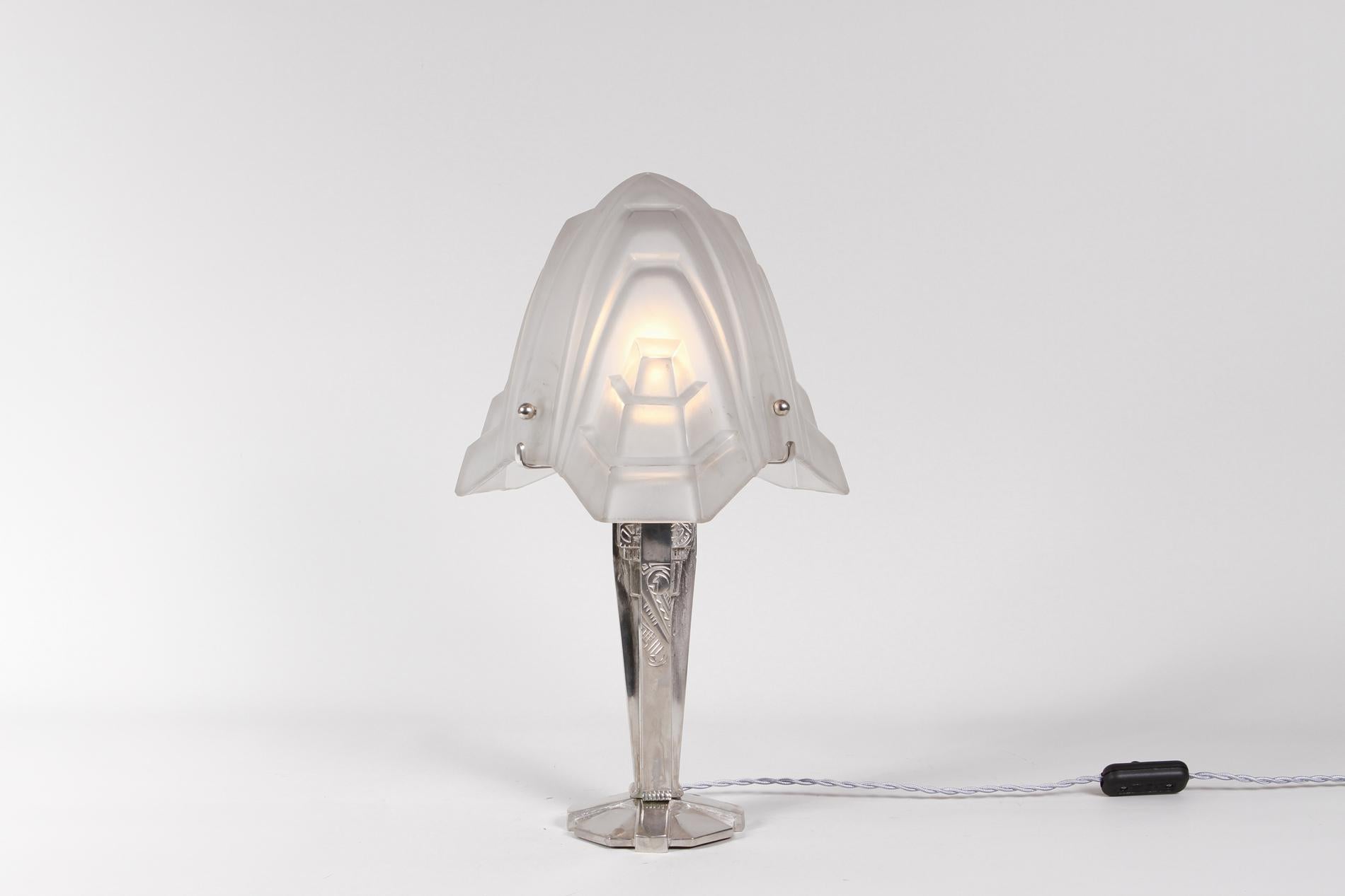French Art Deco table lamp with nickeled bronze for the base and glass lampshade from Degué, 1930. 

The particularity of the lamp is the shape of the glass, designed like a flower and the base with a delicate flower decor bringing elegant light and