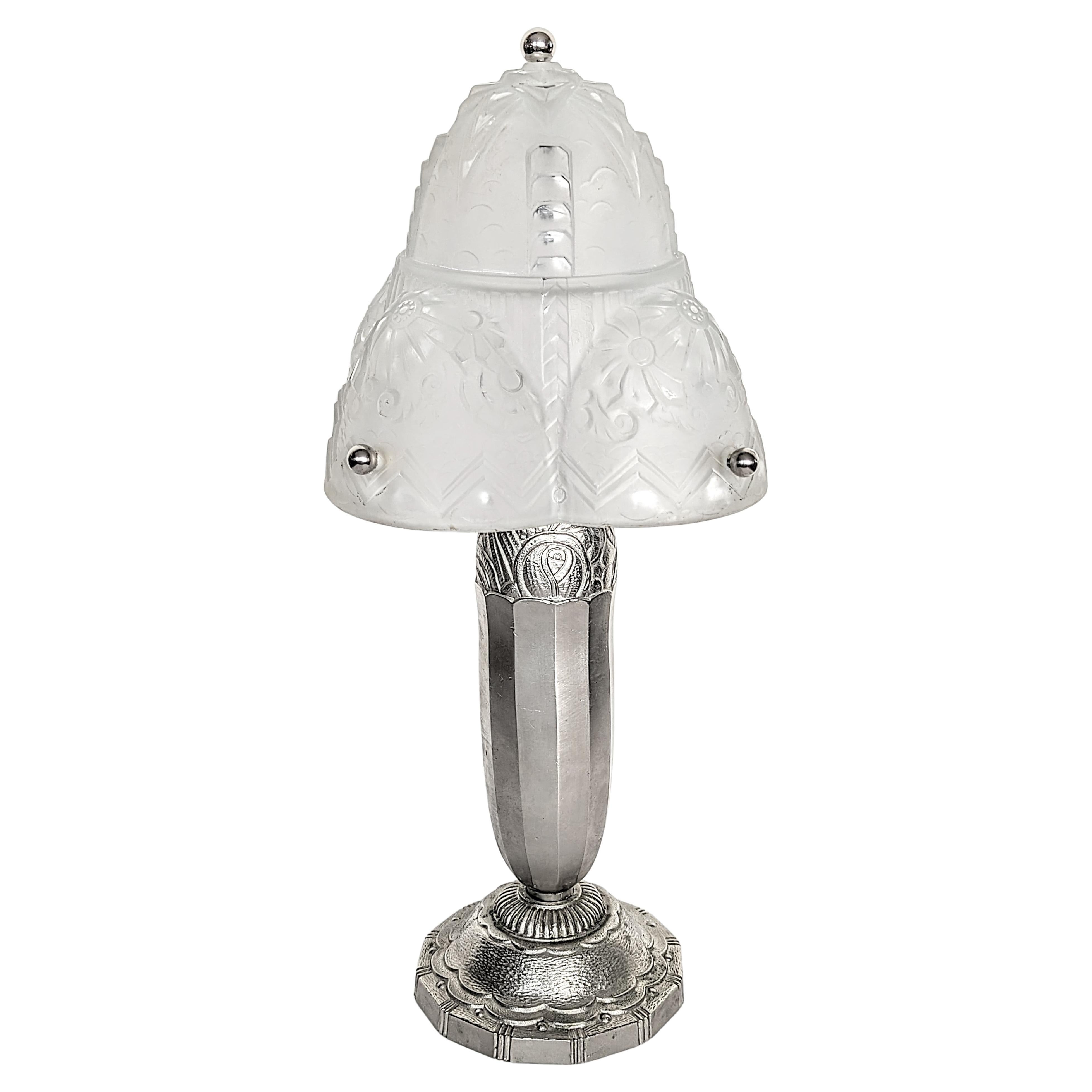A stunning French Art Deco table lamp was created and signed by Muller Frères in great condition. The shade is enhanced by a geometric motif in frosted glass with polished details. Mounted on a Nickeled Bronze with a flower design base. Each lamp