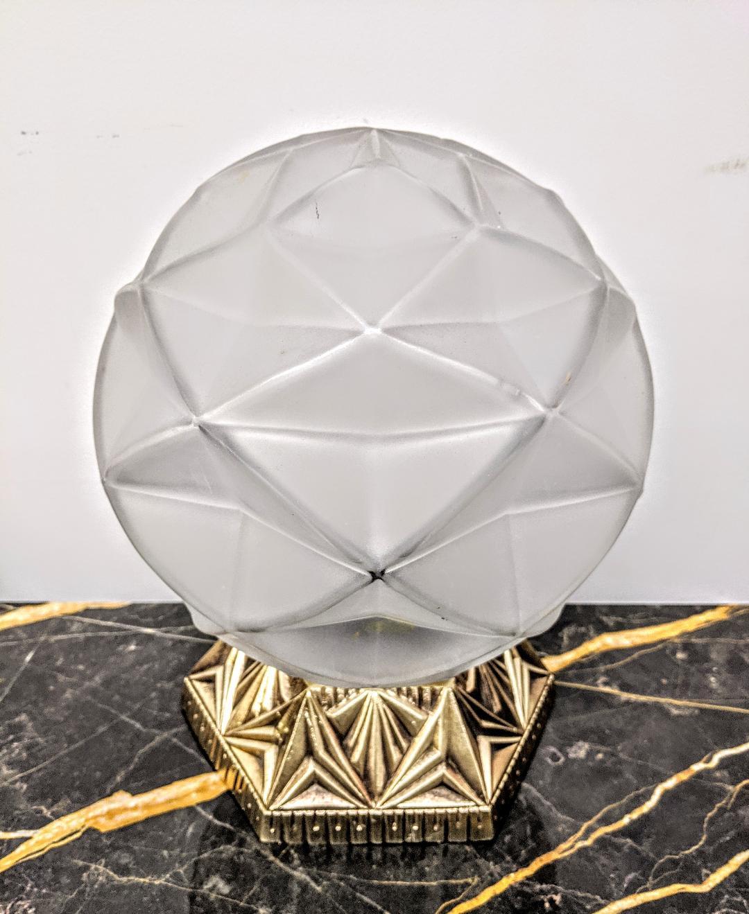 A French Art Deco geometric design table lamp. The glass shade is frosted with polished details in great condition, modest wear commensurate with age. Mounted in a decorative bronze base in its original patina. The table lamp has been rewired for