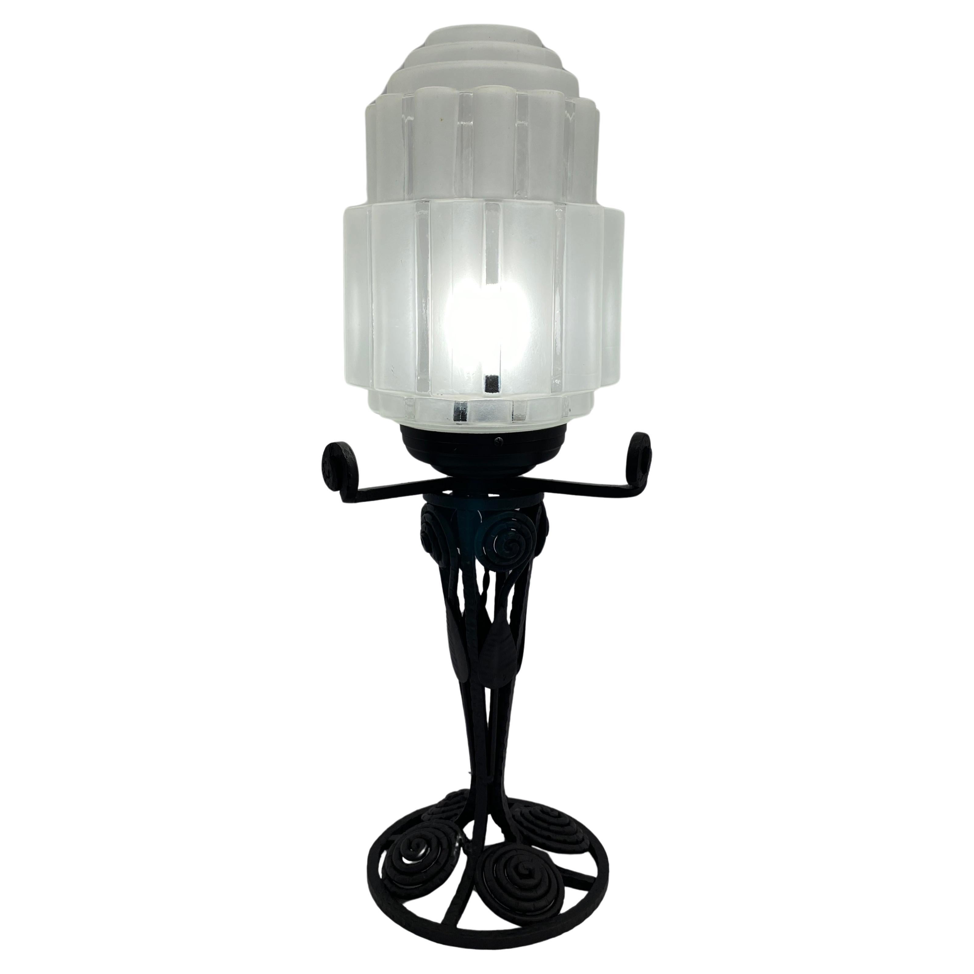 Esta cautivadora Lámpara de mesa Art Déco francesa o Lámpara de mesa Art Déco de hierro y cristal, de hacia 1925, muestra la elegancia intemporal del diseño Art Déco francés. El hierro forjado a mano forma la base, adornada con intrincados detalles.