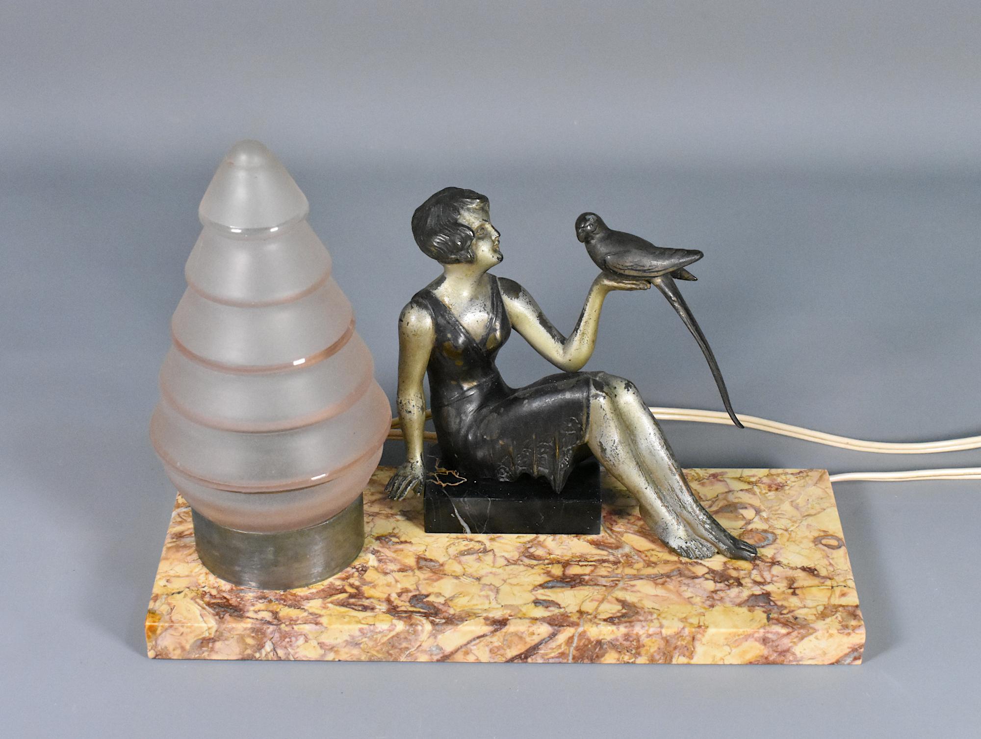 French Art Deco Table Lamp 

A delightful Art Deco Table Lamp featuring a stylish lady, dressed in the fashion of the day with a bob haircut. With her arm outstretched, she holding a bird.  

The spelter lady figurine is sitting on a small portico