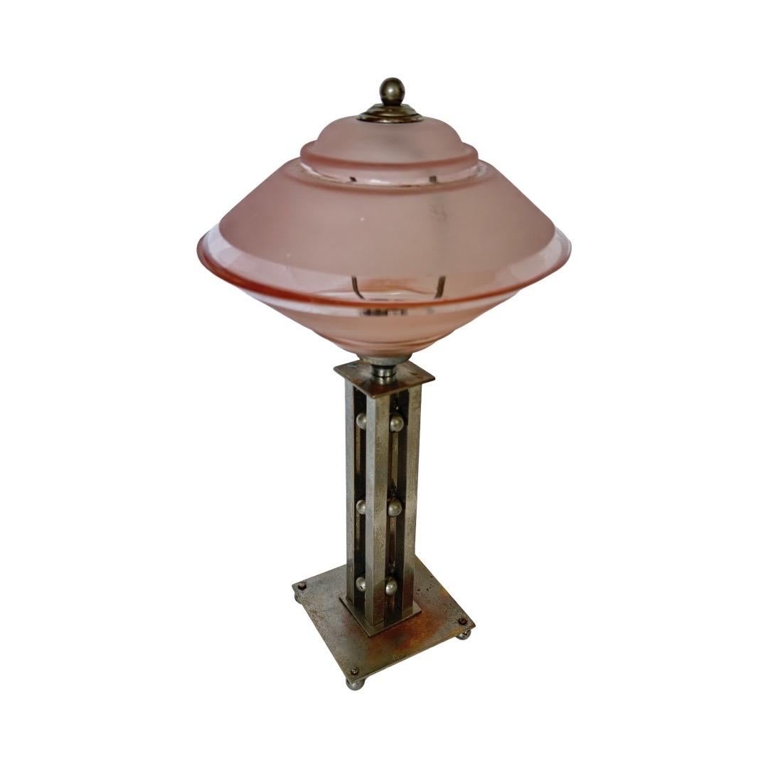Elégante lampe de table Art déco française datant des années 1930. La lampe est dotée d'un abat-jour en verre rose dépoli de forme étonnante, associé à une base géométrique architecturale en métal ornée de sphères décoratives. Cette fusion de