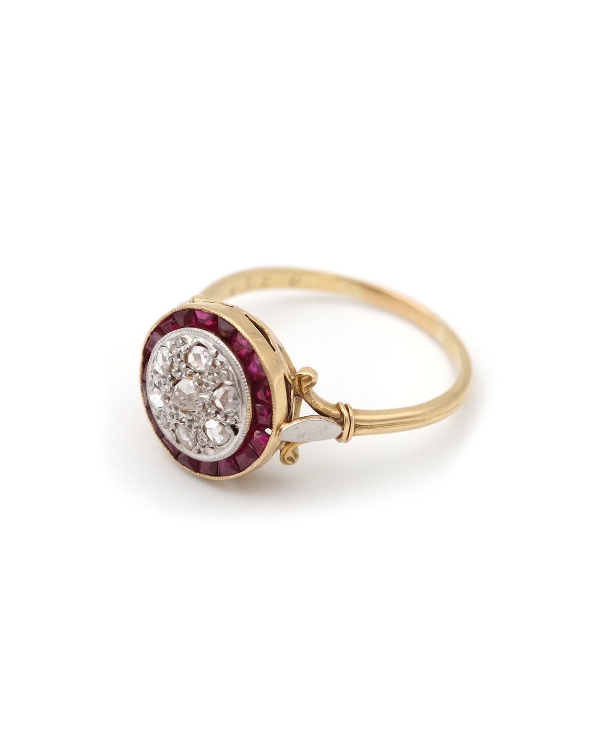 French Art Deco target ruby ring in 18 karat gold and platinum. A round-shaped ring from the 1930s, set in its center with seven rose-cut diamonds, surrounded by calibrated synthetic rubies. The shoulders of the ring are decorated with a thin,