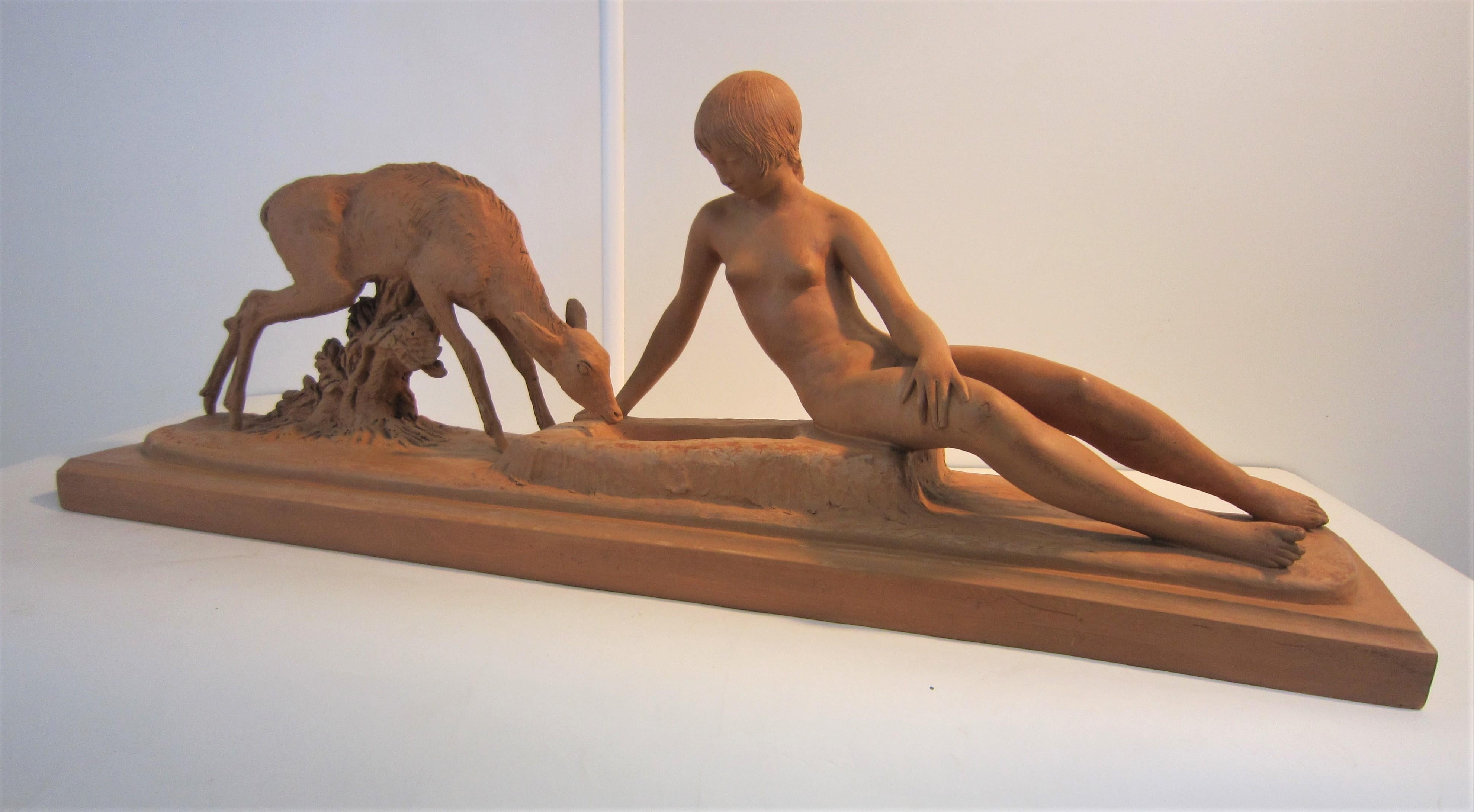 A fine signed original French Art Deco terracotta sculpture of a naked young woman seated on a rectangular shaped self plinth. The bare chested female figure in a semi reclining pose is portrayed with a fawn drinking out of a trough by her