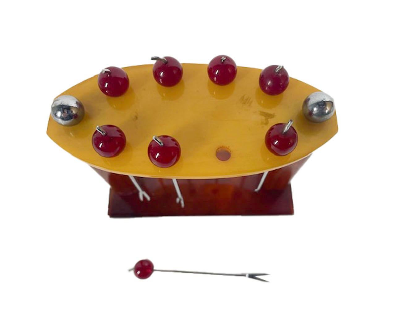 French Art Deco cocktail picks and stand. Eight chrome plated forked picks with translucent red cherry tops in a faux tortoise Bakelite stand with pierced butterscotch Bakelite top-plate held in place with chromed ball finials.