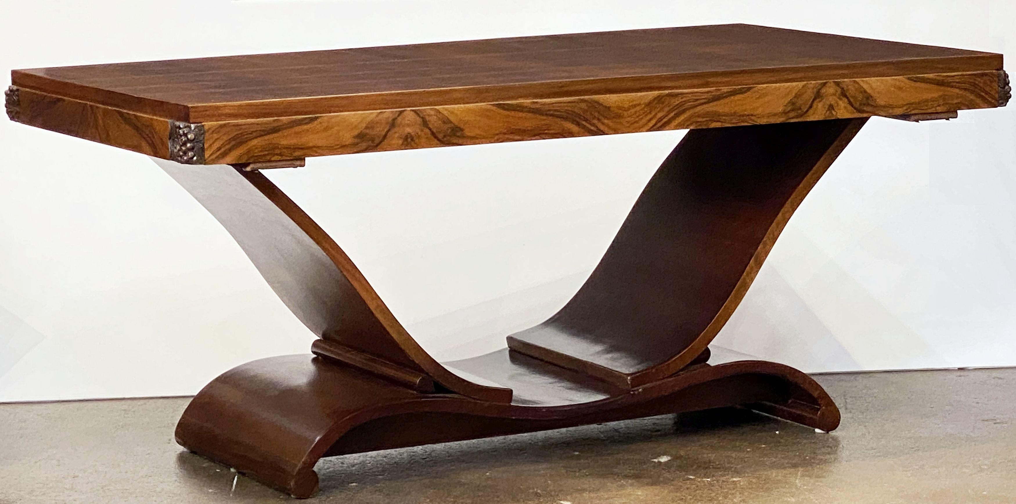 A fine French dining table from the Art Deco era, featuring a walnut top set upon on a u-shaped base, in figured and cross-banded walnut with hand-carved foliate decoration to the corners, and two opposing pull-out pitch pine table