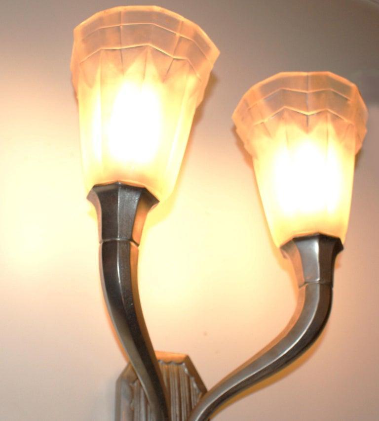 Superbe scone mural Art Déco français signé Degué (David Gueron) sur le verre, comportant chacun deux tulipes en verre clair dépoli moulé et tenues par deux bras en bronze nickelé à motif géométrique.
Avec deux douilles candélabres pour un total de