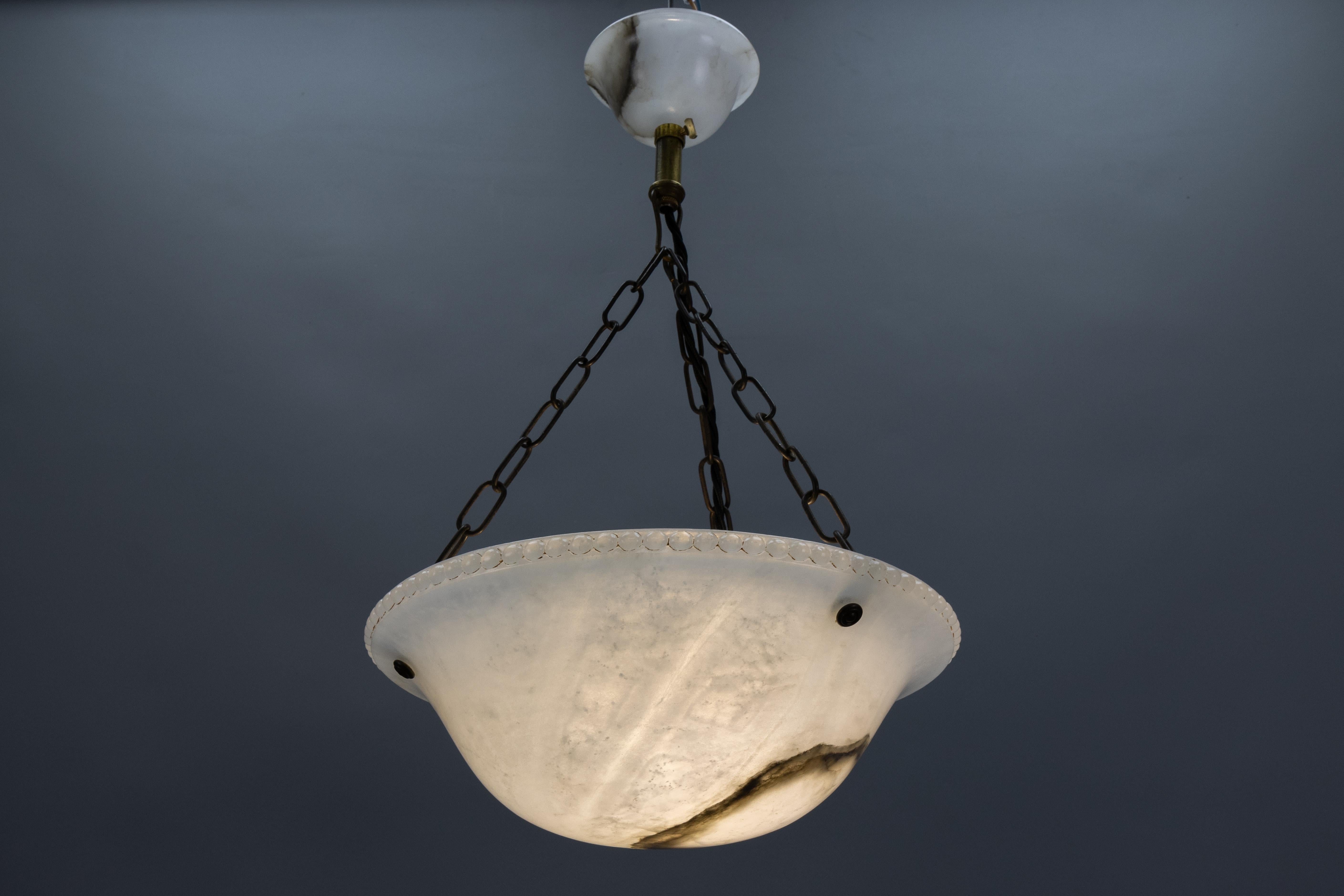 Antique Art Deco white alabaster pendant light fixture with dark brown and black veins.
Adorable and compact-sized alabaster pendant ceiling light fixture from circa 1920. This beautifully veined and shaped white alabaster bowl is suspended by three