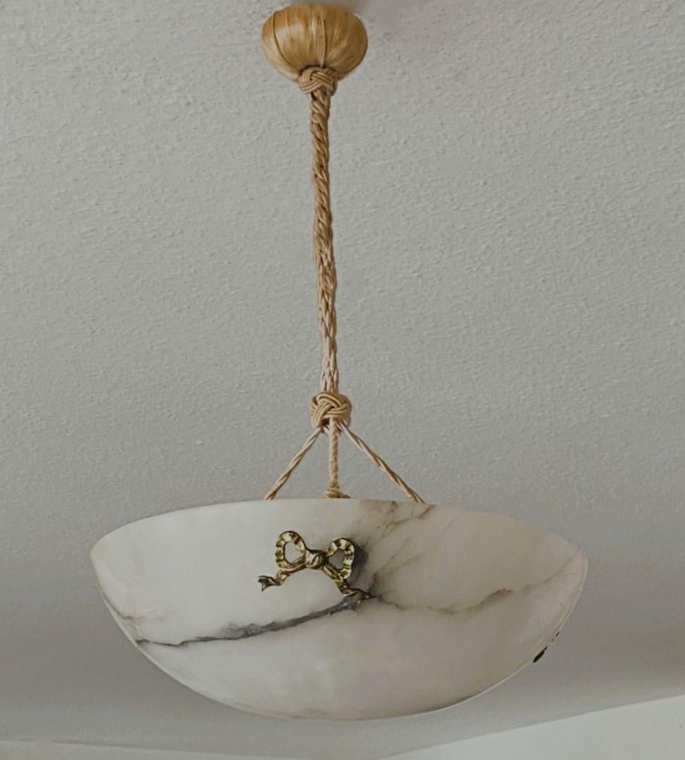 A lovery Arte Deco era alabaster pendant / light fixture, France, 1930-1939. Hand-carved shade from a solid alabaster rock with beautiful black veining and polished to a natural shine. Suspended from three original hand-knotted ropes connecting to a