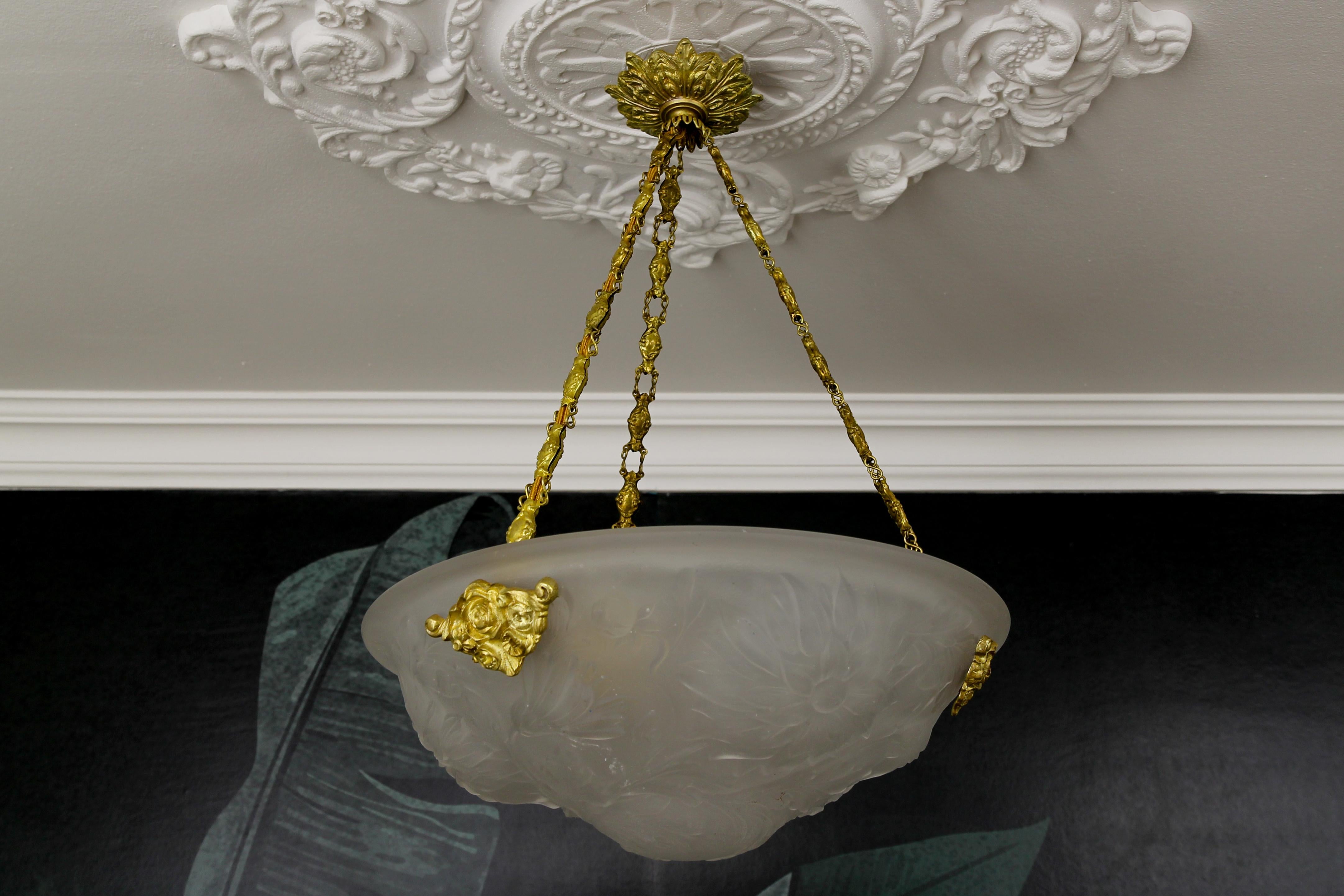 A beautiful French Art Deco single-light pendant light fixture with white frosted glass shade from circa the 1930s.
This beautifully shaped white frosted glass bowl features floral motifs hung at three decorative chains, attached with adorable