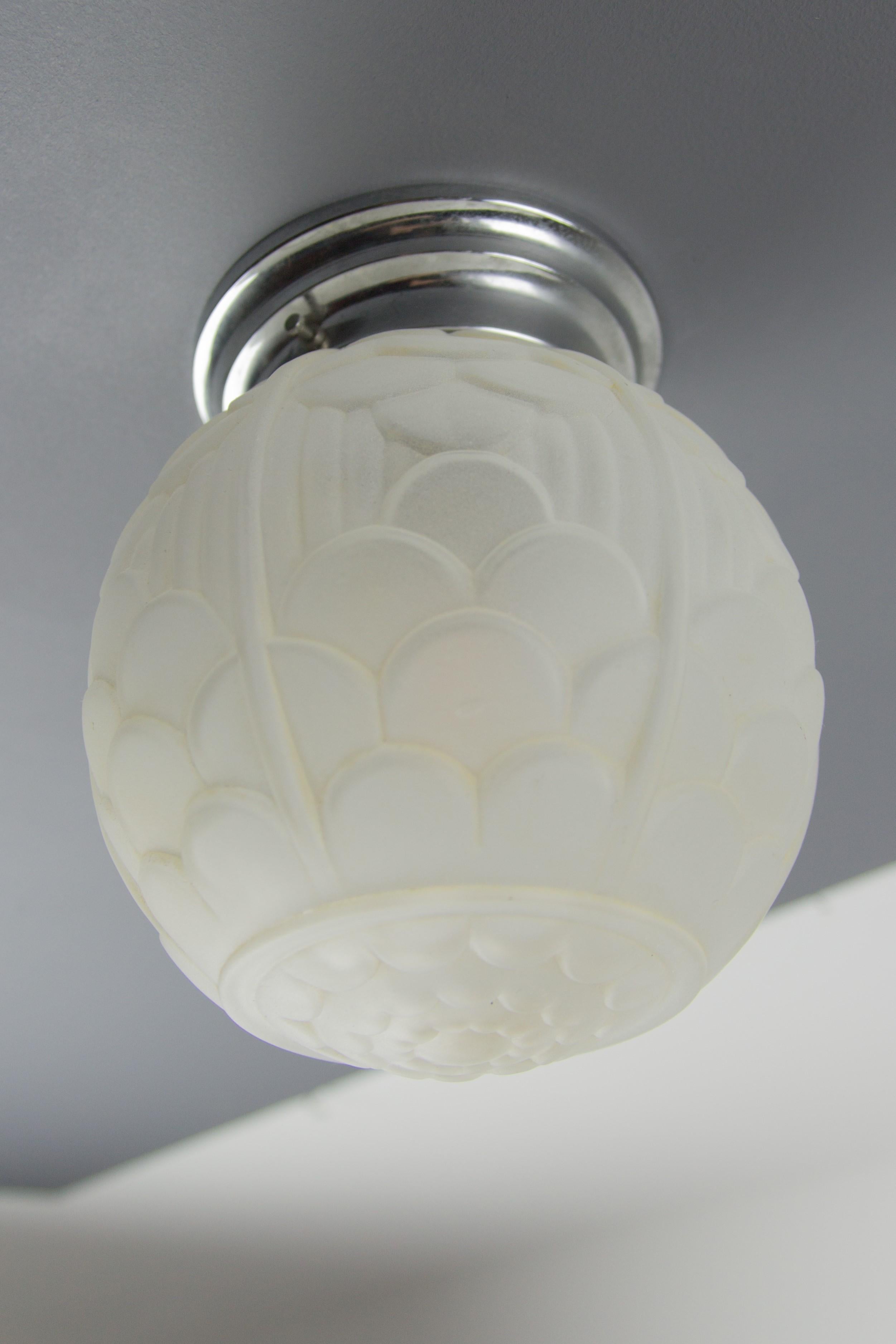 This adorable French ceiling light fixture features white frosted pressed glass with stylized geometrical floral motif, typical for Art Deco period. Chrome-plated metal mount for attaching to the ceiling. Newly rewired, one socket for B22 light