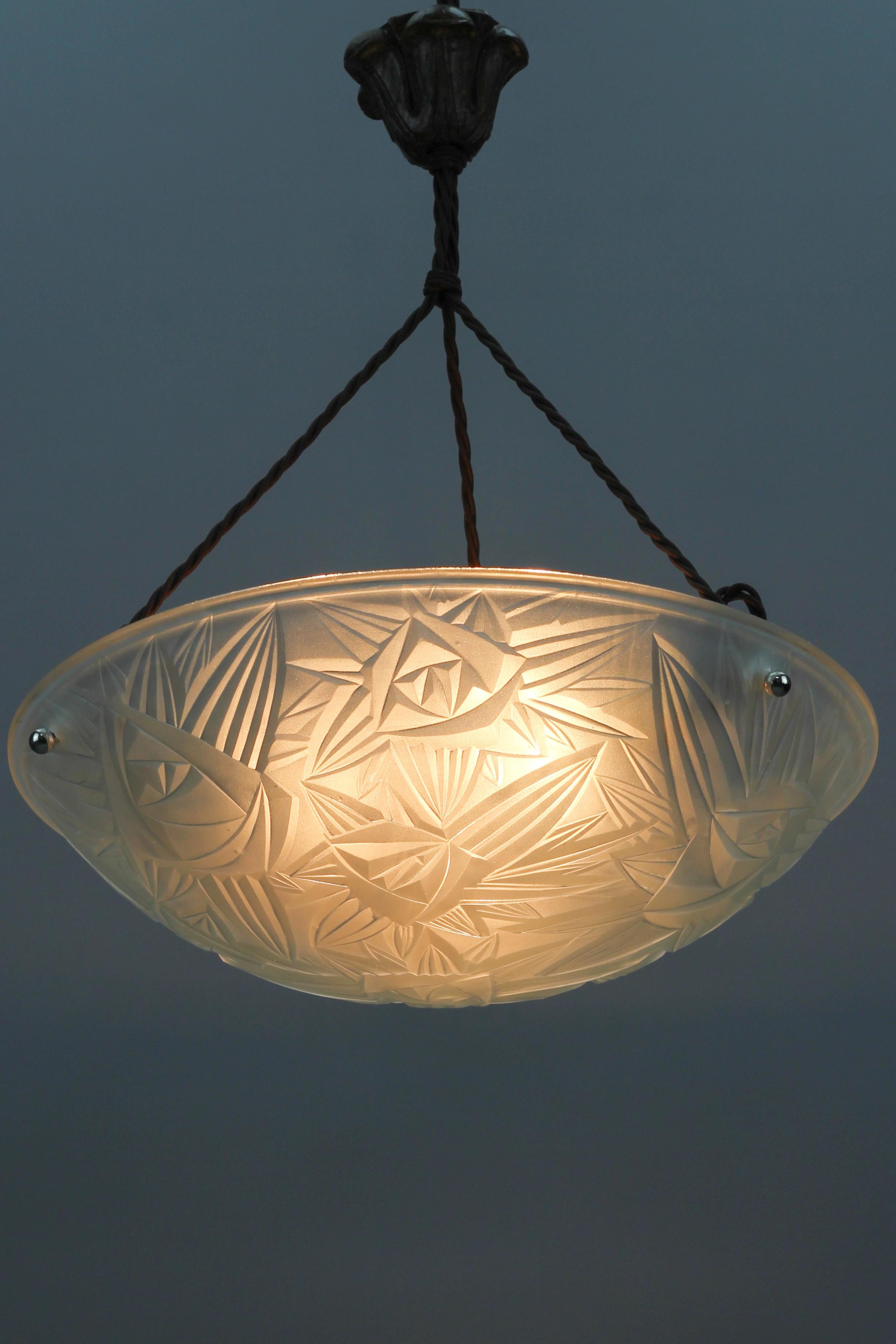 Beautiful French Art Deco three-light pendant light fixture with frosted pressed glass shade by Jean Noverdy; marked on edge ”Noverdy France Depose”.
Beautifully shaped white frosted glass bowl features stylized flower and leaf decoration, hung at