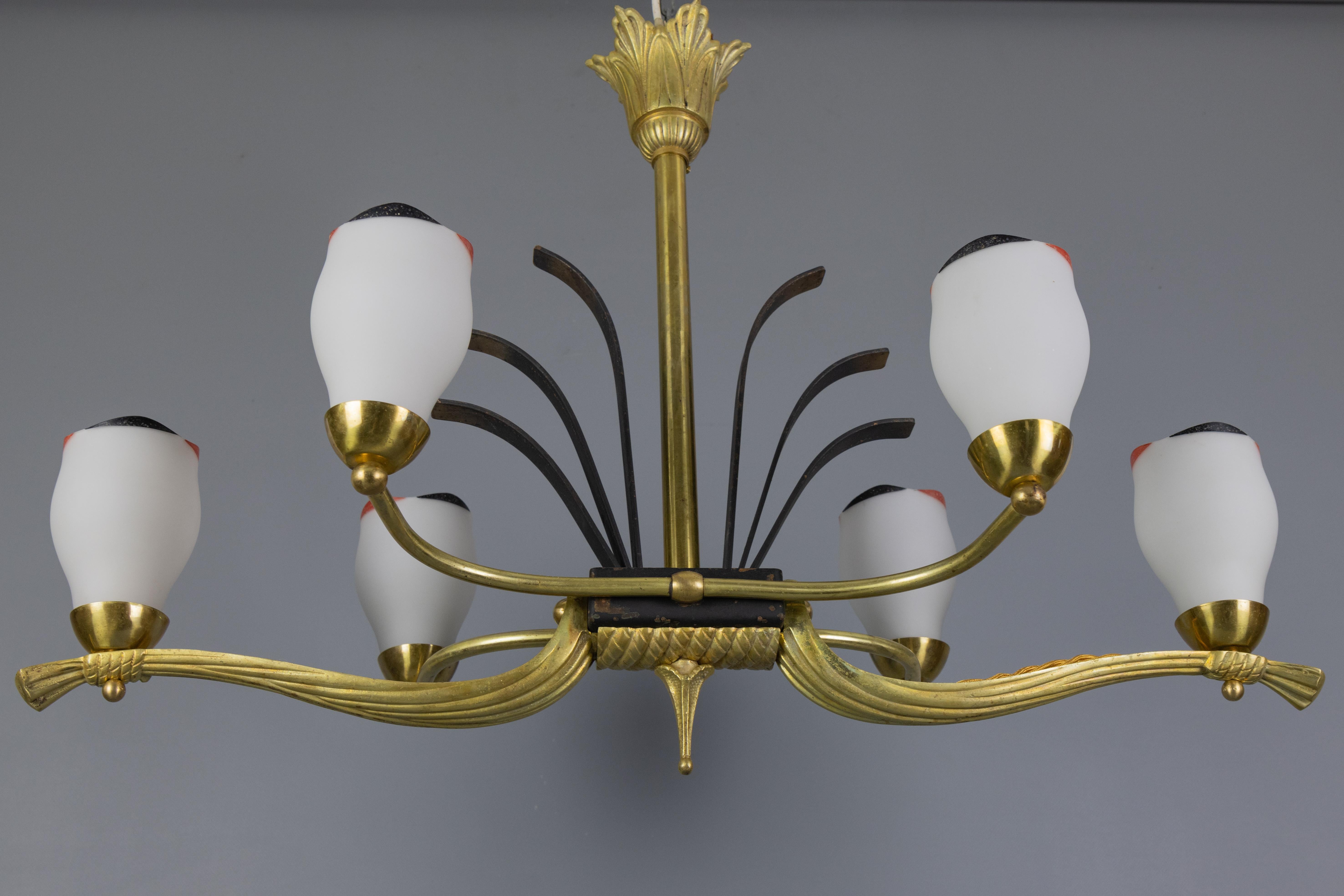 French Art Deco White Glass, Bronze, Brass, and Iron Six-Light Chandelier from the 1920s.
This exceptional Art Deco chandelier features an elegant bronze, brass, and black-painted iron frame with six light points: six white glass lampshades with red