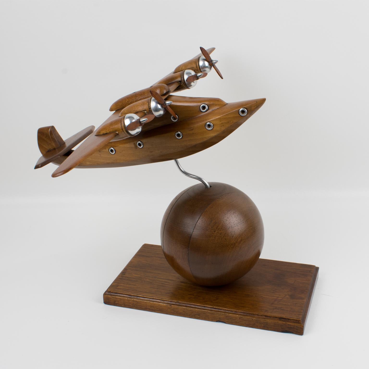 French Art Deco wooden airplane model mounted on a huge wood ball. This large Art Deco model airplane is made with varnish wood and aluminum metal accents. It has four wood and aluminum propellers. Standing on a carved wood plinth which the plane