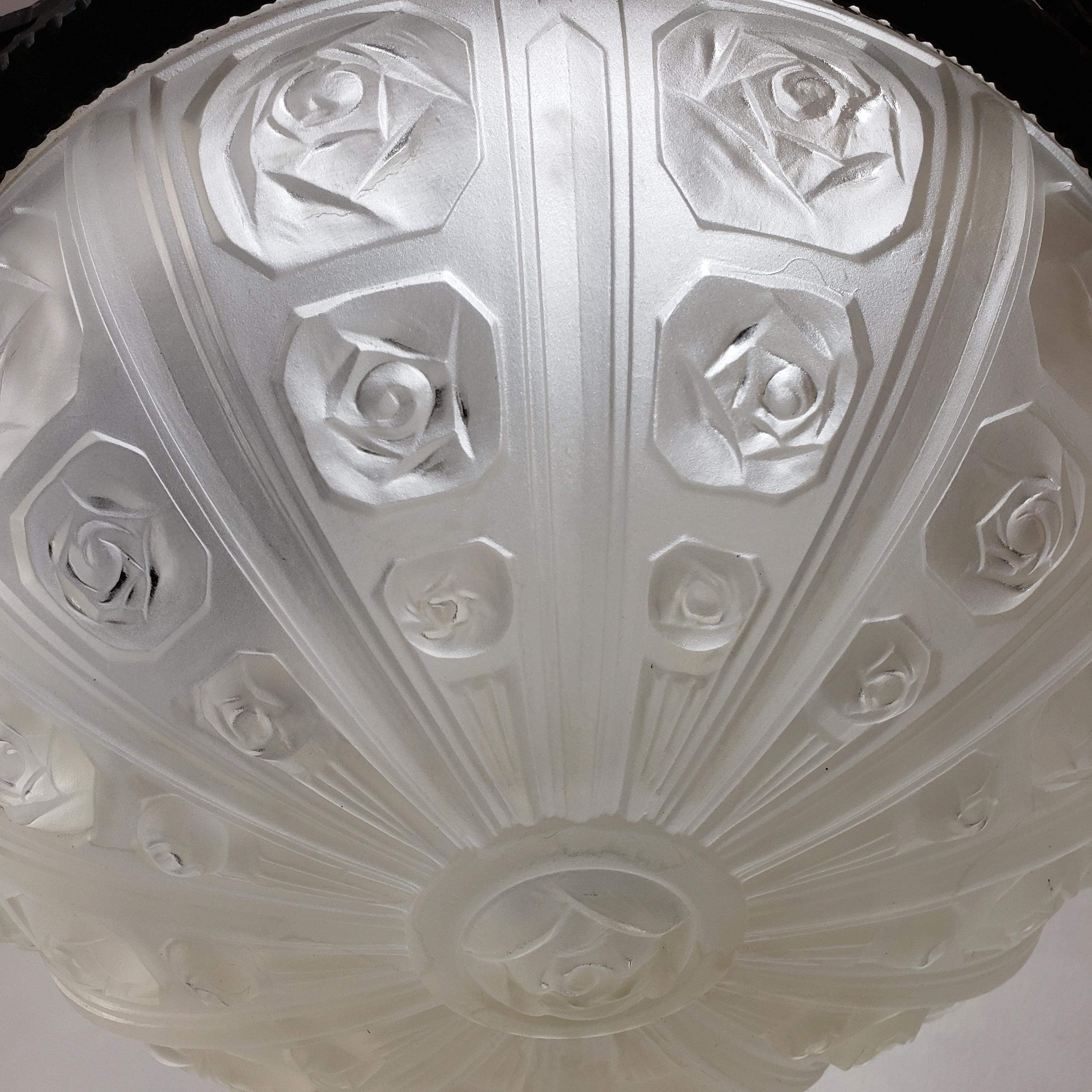 French Art Deco chandelier featuring a floral themed relief frosted glass bowl in the center and three matching shades. It has a highly stylized wrought iron frame with sleek geometric accents typical of the Art Deco period. The wiring is relatively