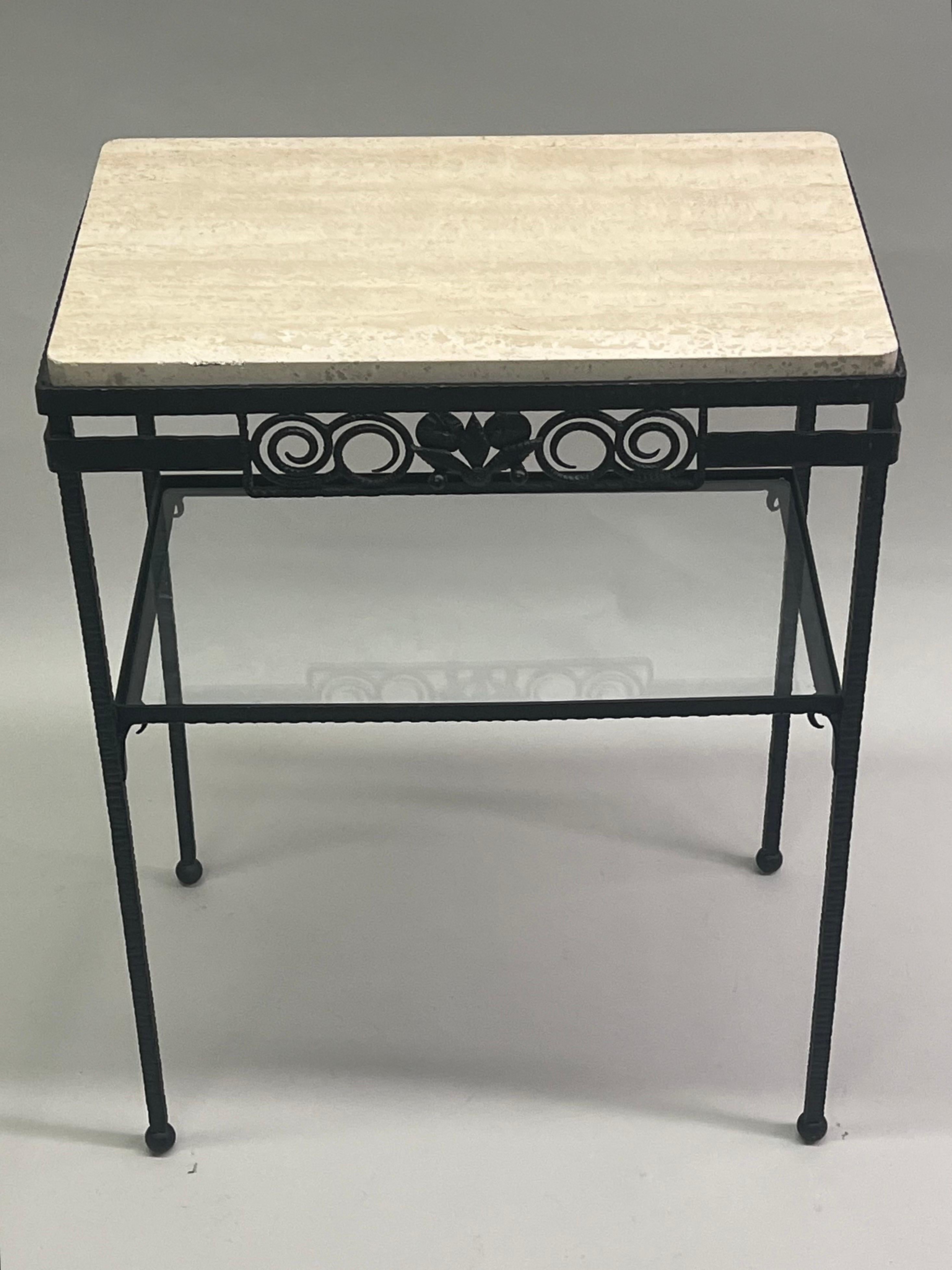 A Rare and Elegant double tier French Mid-century / Art Deco console, side table or nightstand attributed to Edgar Brandt. The piece is composed of hand-hammered wrought iron with a top of travertine and lower level of glass. The table is a work of