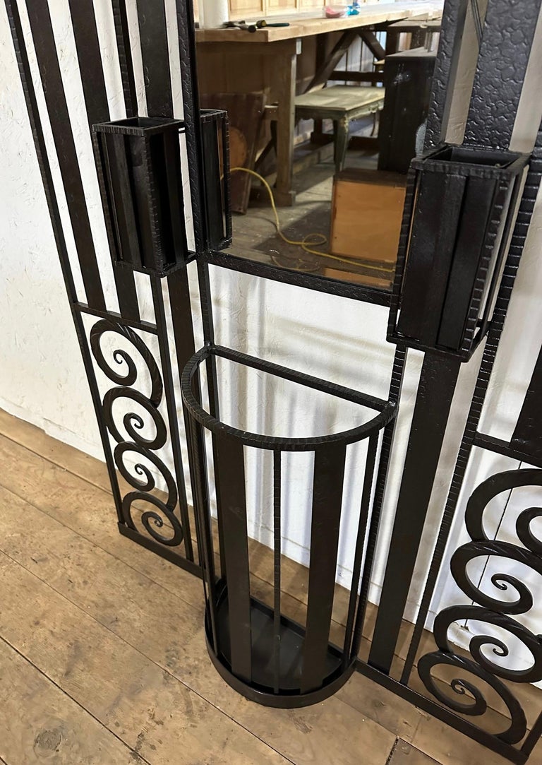 A Fine example of a Classic 1930s French Art Deco wrought iron foyer coat rack or hall tree is wonderfully decorated with geometric and circular iron work, two electrified lights with round frosted glass cover, an overhead shelf, four coat hooks, an