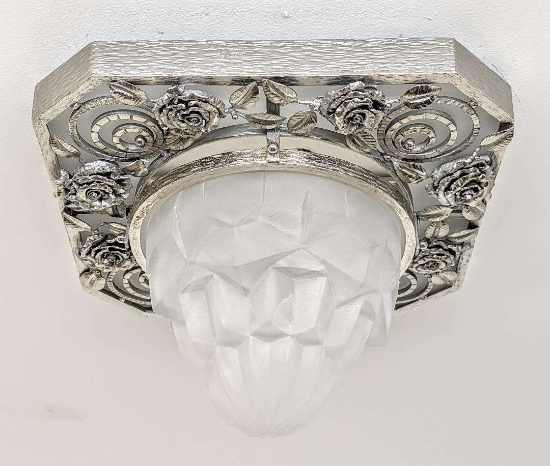 
A French Art Deco wrought iron hammered flush mount enhanced by different textures with flower leaves detail. Accommodating a round center coupe in clear frosted molded shade in a geometric motif. The fixture is in great condition with modest wear
