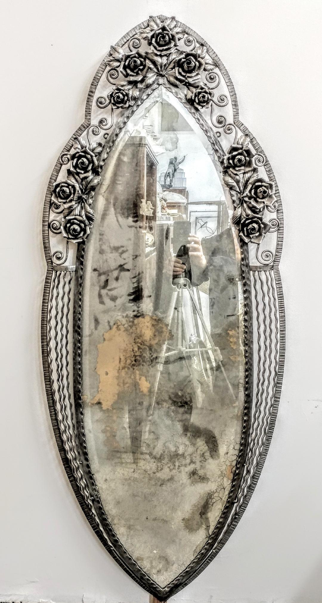Ein majestätischer französischer Art-Déco-Spiegel in ovaler Form aus Schmiedeeisen, umgeben von verschlungenen Blumen und Blättern. Schriftrollen mit glatter und gehämmerter Textur. Ein neuer Spiegel wird mitgeliefert. Kostenlose Abholung im