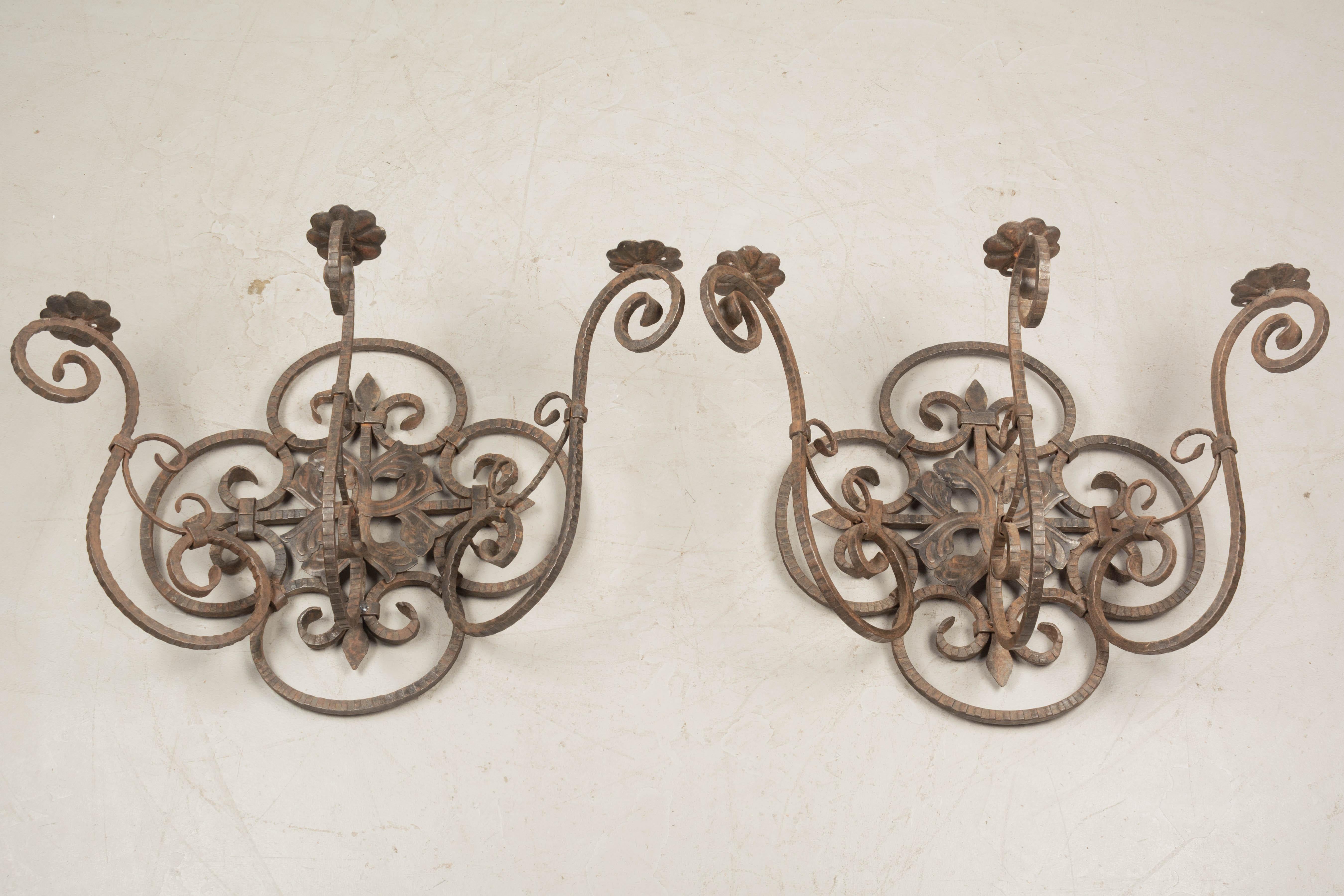 A pair of large French wrought iron and tôle three-light candle sconces with scroll form and rusty bronze patina. Good quality ironwork with nice aged patina. Not wired. Two arms have been repaired. Circa 1920s. 
Dimensions: 29.5
