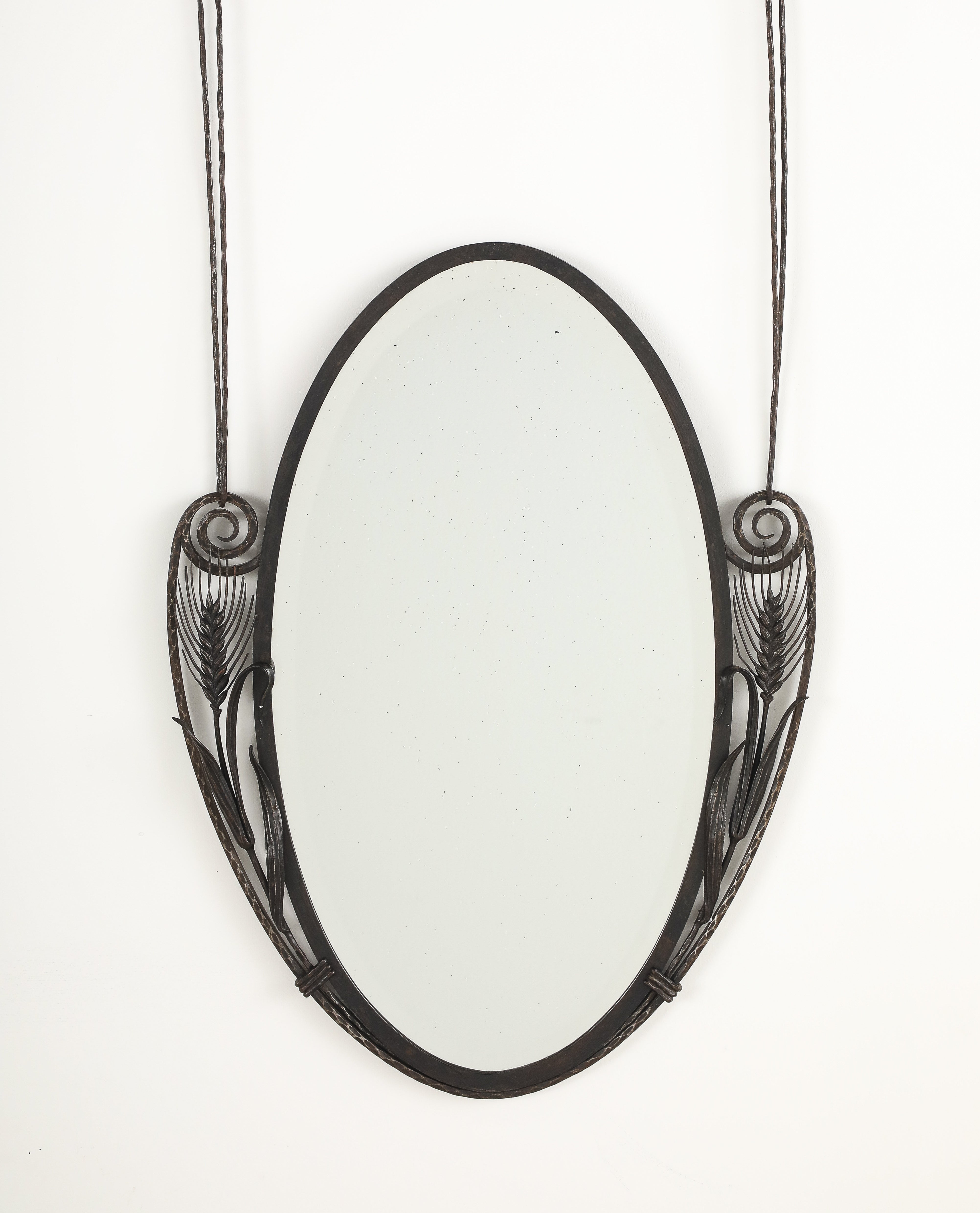 A French Art Deco wrought iron wall mirror with wheat and fanciful scroll motif and beveled glass; with wrought iron hanging supports; of majestic form and presence.  
Francia, 1925 circa 
Size: 50