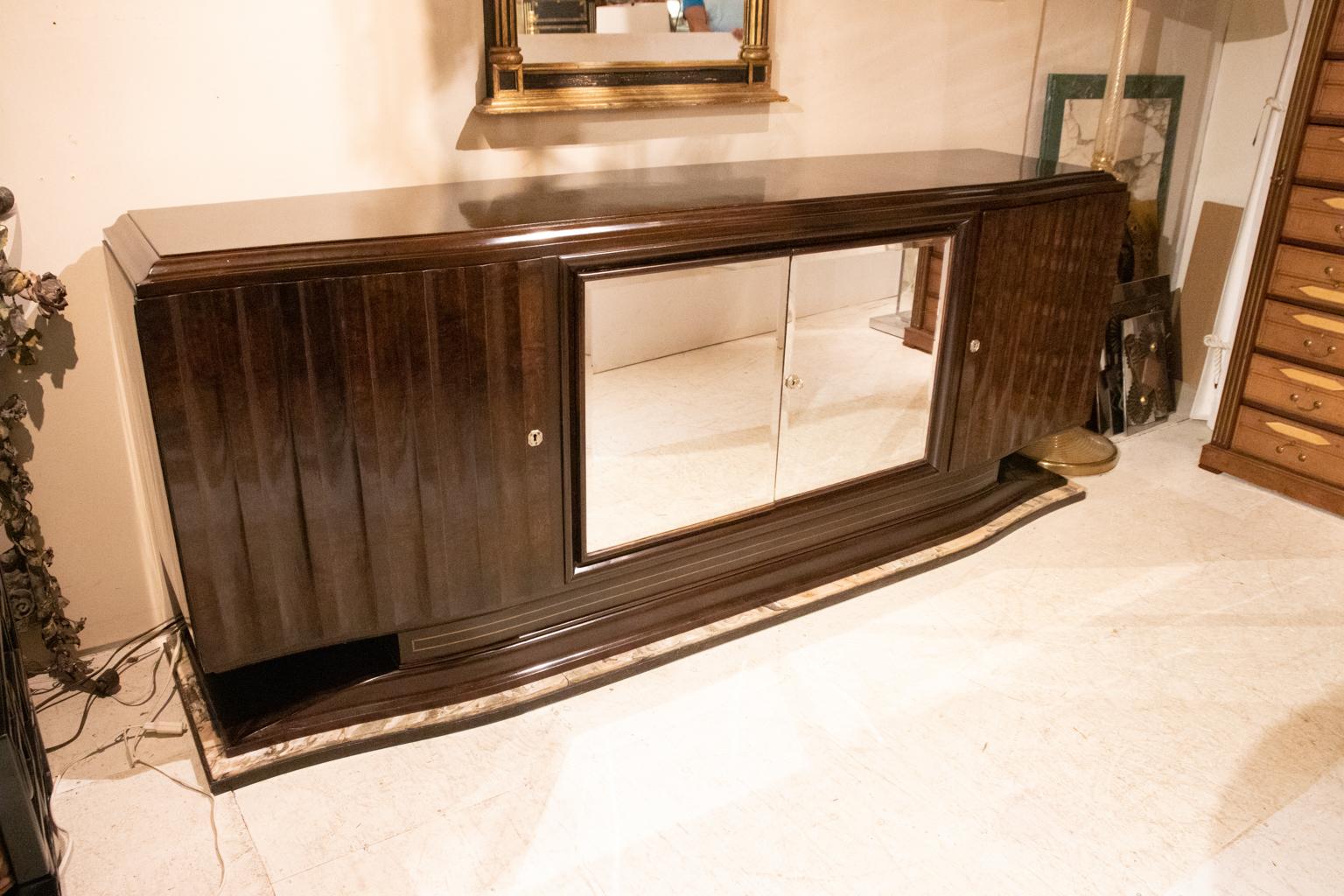 French art moderne credenza of highly polished rosewood with a pair of mirror doors flanked on each side by a polished wood door, circa 1930s. The credenza tapers to a base of wood and marble. The top is also highly polished. The interior of this