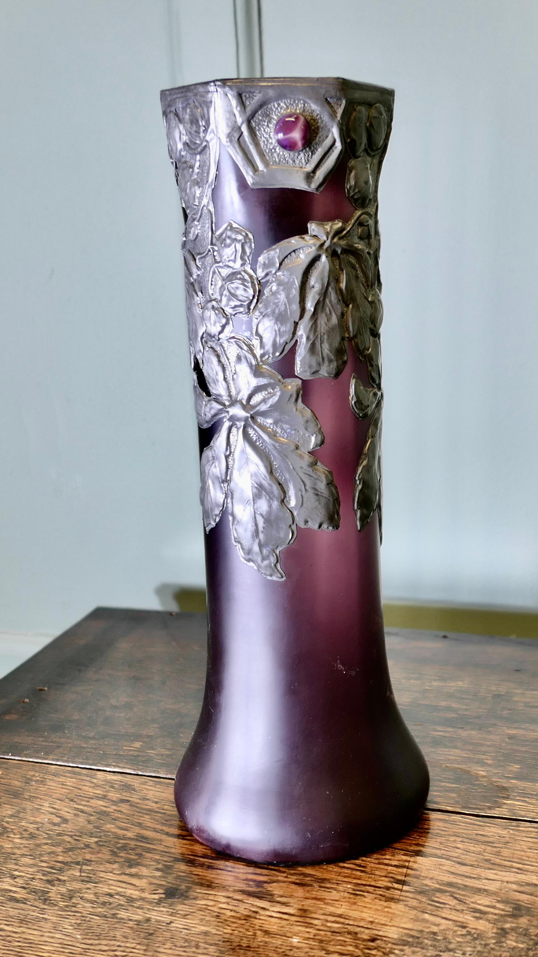 French Art Nouveau Amethyst Vase with Pewter Overlay

Tall Aesthetic amethyst glass vase overlayed with pewter, a floral design and inset with iridescent violet cabochon.  
This is an excellent early 20th Century piece from France, it is 16” tall