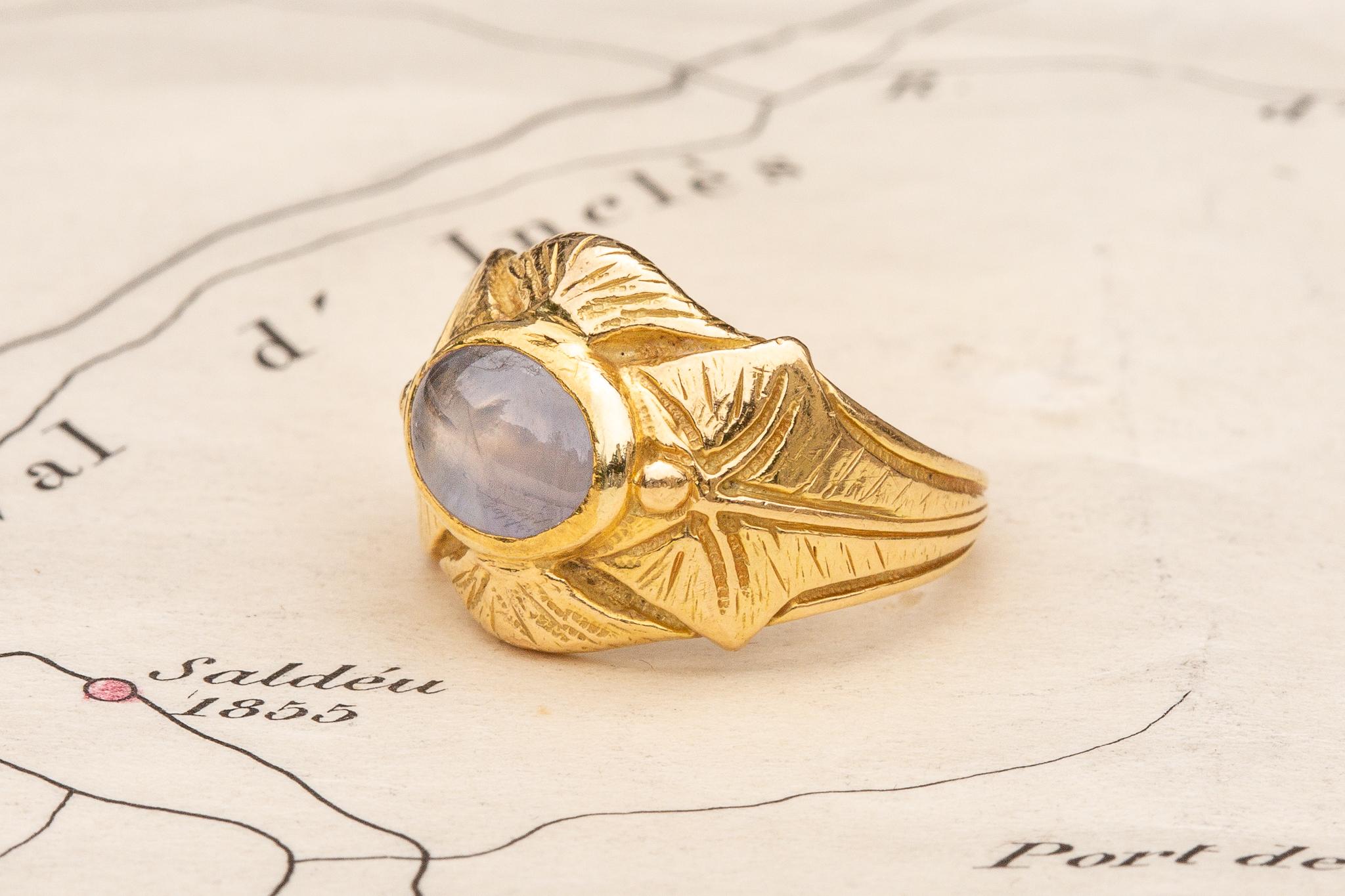 A gorgeous antique French Art Nouveau figural ring made in Paris, circa 1900. The ring is crafted in 18K yellow gold and features an 1.63ct star sapphire. 

The milky spheroid shaped lilac ‘star sapphire’ displays asterism, a rare optical phenomenon