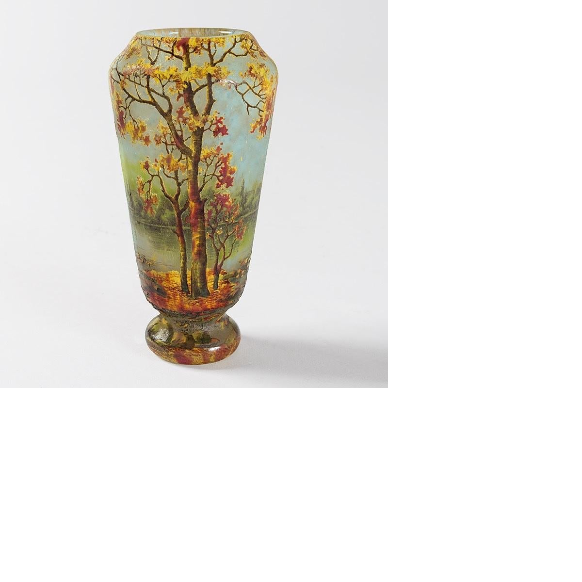 A French Art Nouveau vase by Daum featuring a forest scene in vitrified glass. The intricate scene on this vase has components that together form an autumnal landscape. The ground is largely made up of a central band of orange that flows into the