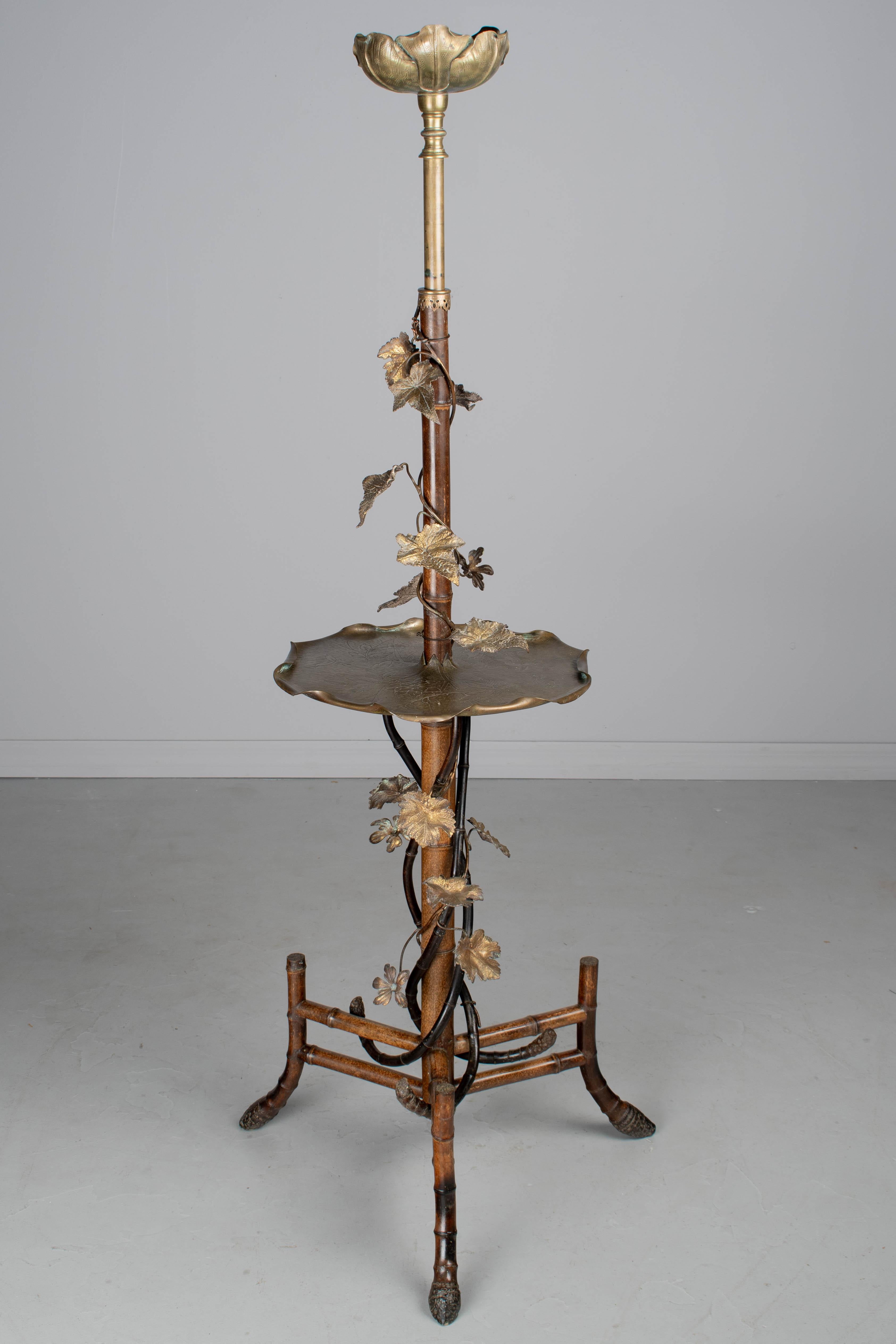 Lámpara de pie Art Nouveau Aesthetic Movement francesa de finales del siglo XIX con mesa circular de latón. Robusta construcción de bambú con mástil central y base de trípode con extremos de raíz en los pies. Enredadera de bambú ebonizado con hojas