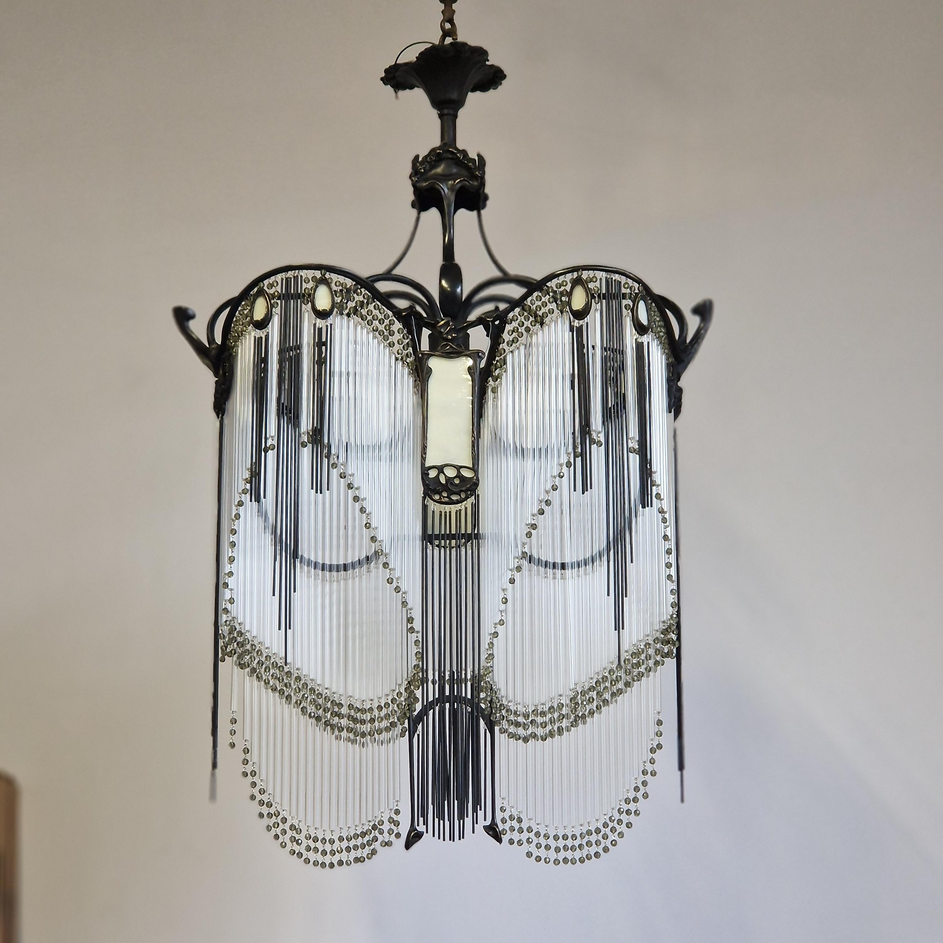 Immergiti nell'eleganza dell'Art Nouveau con questo sontuoso lampadario Guimard, un vero capolavoro che unisce finezza e raffinatezza. Realizzato in bronzo ossidato annerito a fiamma, rivela curve organiche e una struttura fluida, caratteristica