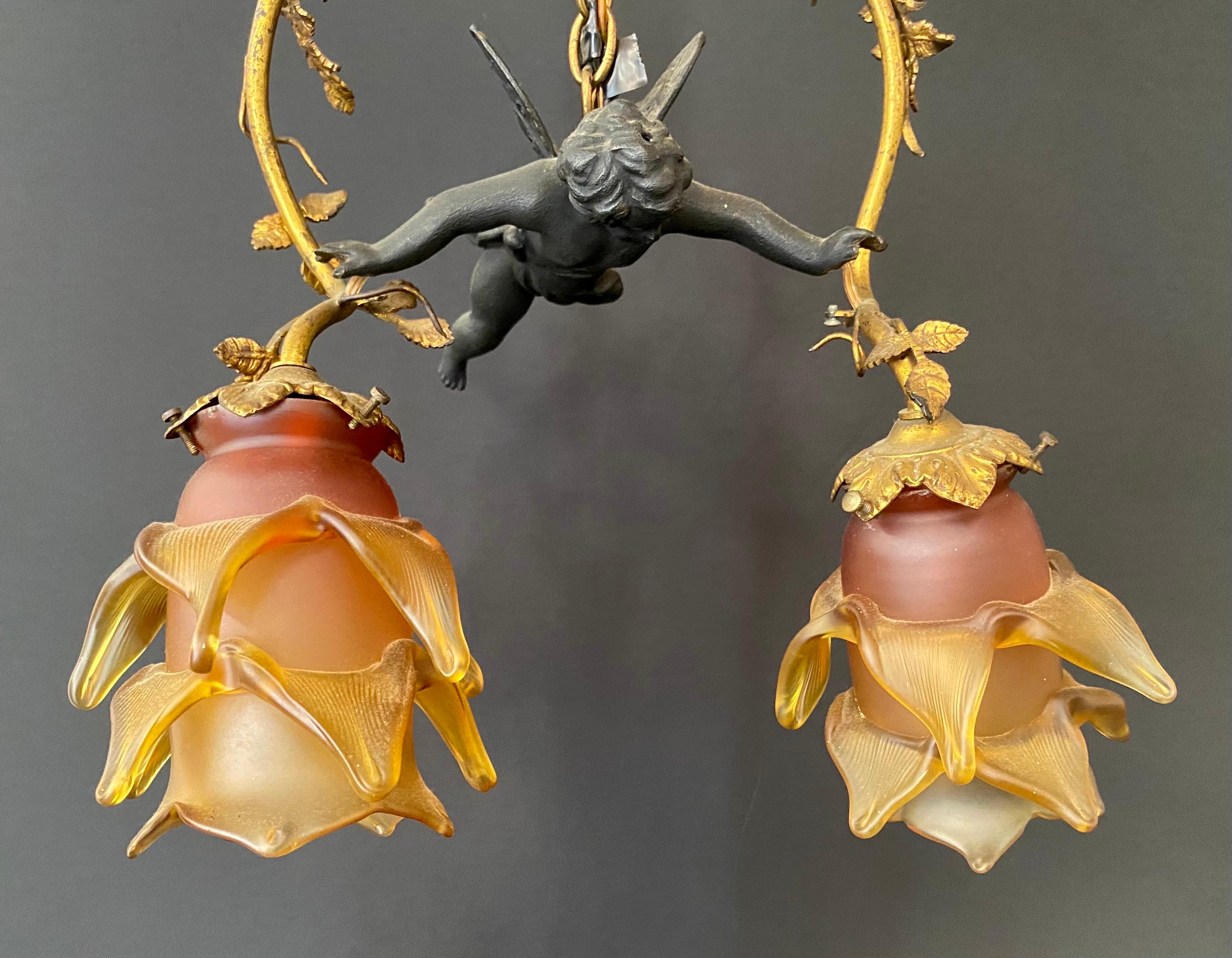 A marvelous French art nouveau flying putto cherub chandelier or pendant. The two light chandelier features a putto holding a beautiful brass arch embellished classical art nouveau leaves with  two rose and gold frosted glass Lalique style  tulip