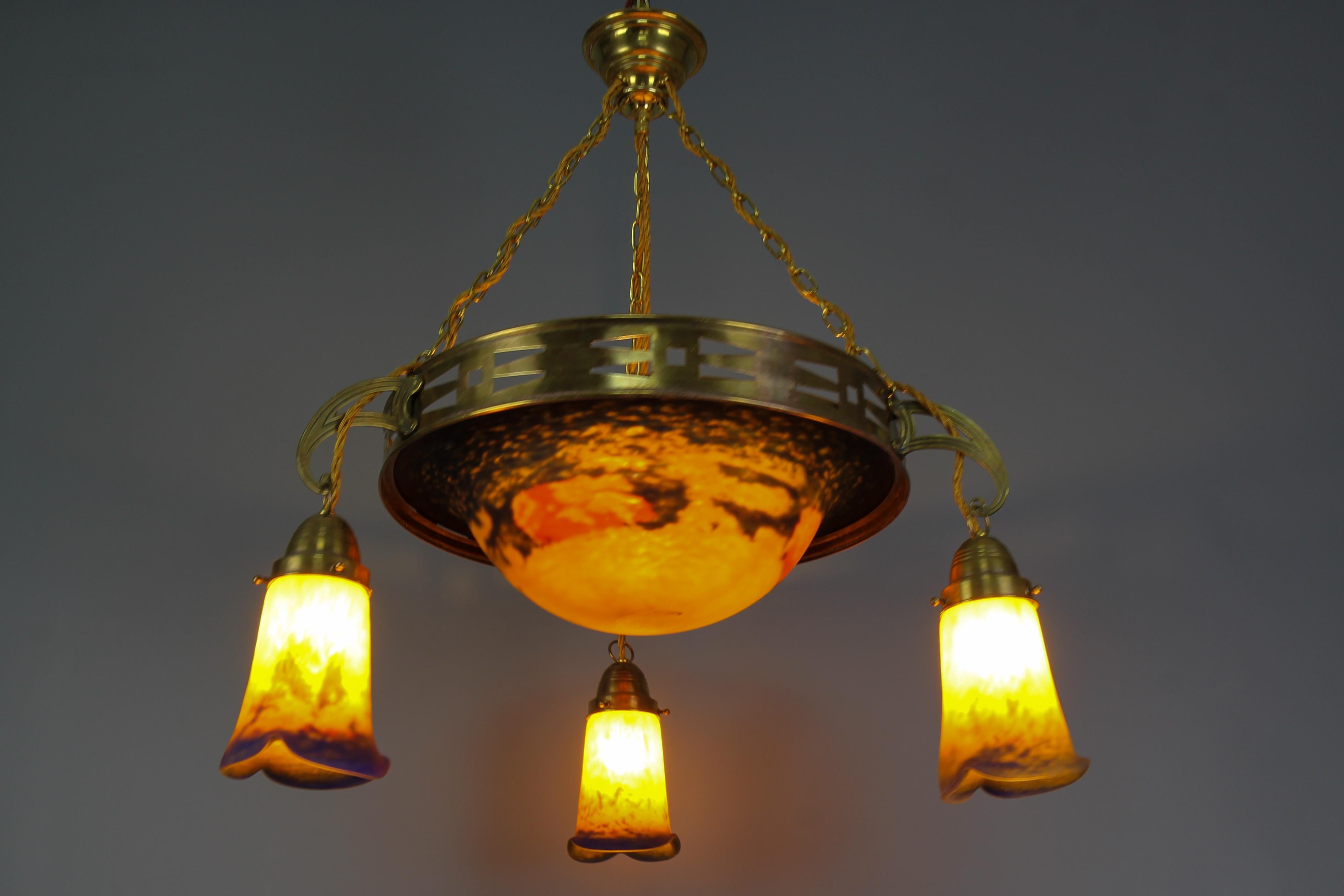A beautiful four-light Art Nouveau brass pendant chandelier with Pâte de Verre glass by Noverdy.
This impressive French Art Nouveau period chandelier features a central, beautifully shaped “Pâte de Verre” glass bowl in dark yellow, red, and blue