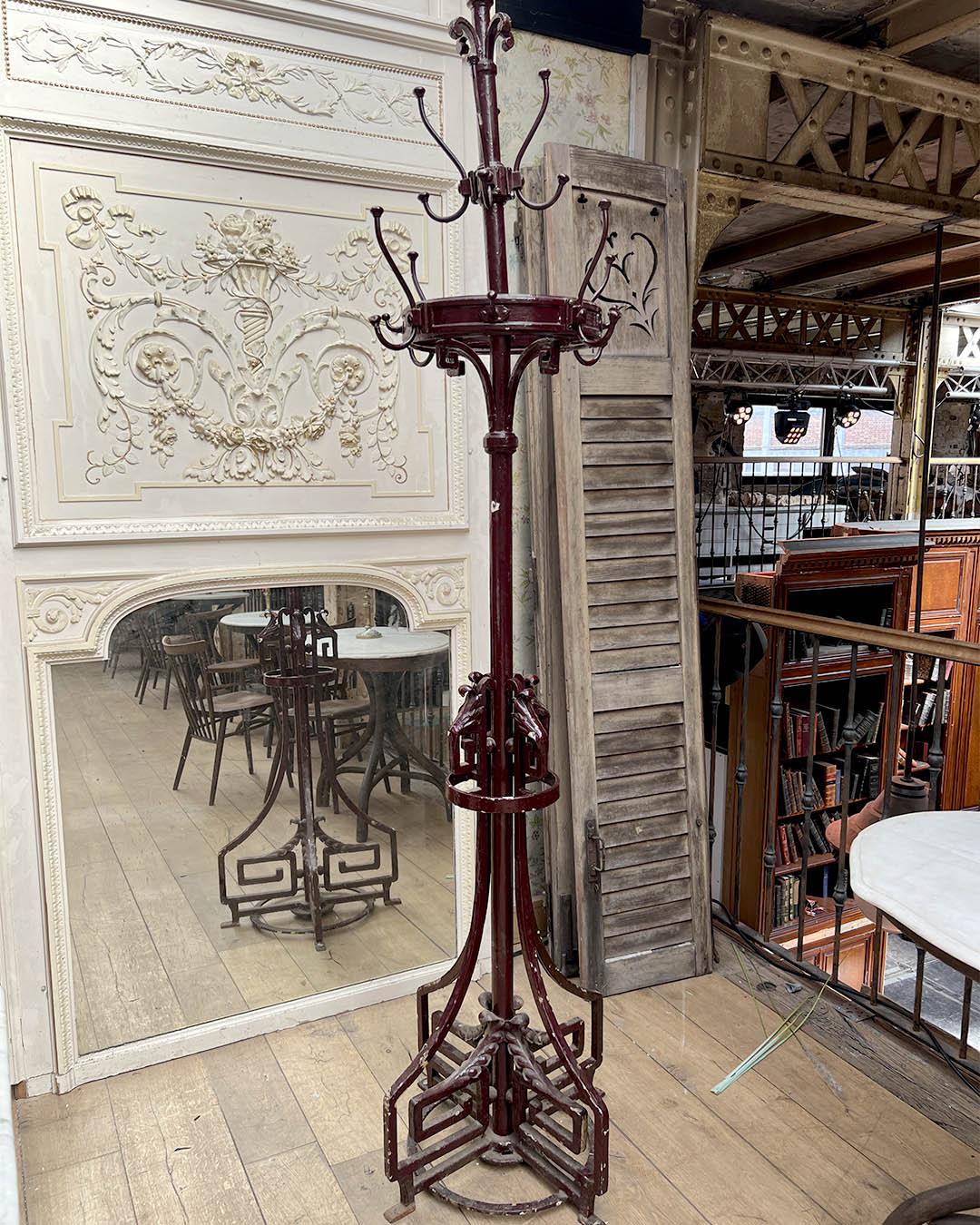 This impressive Art Nouveau coat rack features a solid cast iron structure with elegant organic lines and intricate detailing, characteristic of the early 20th-century French decorative style. The rich burgundy finish highlights the sculptural