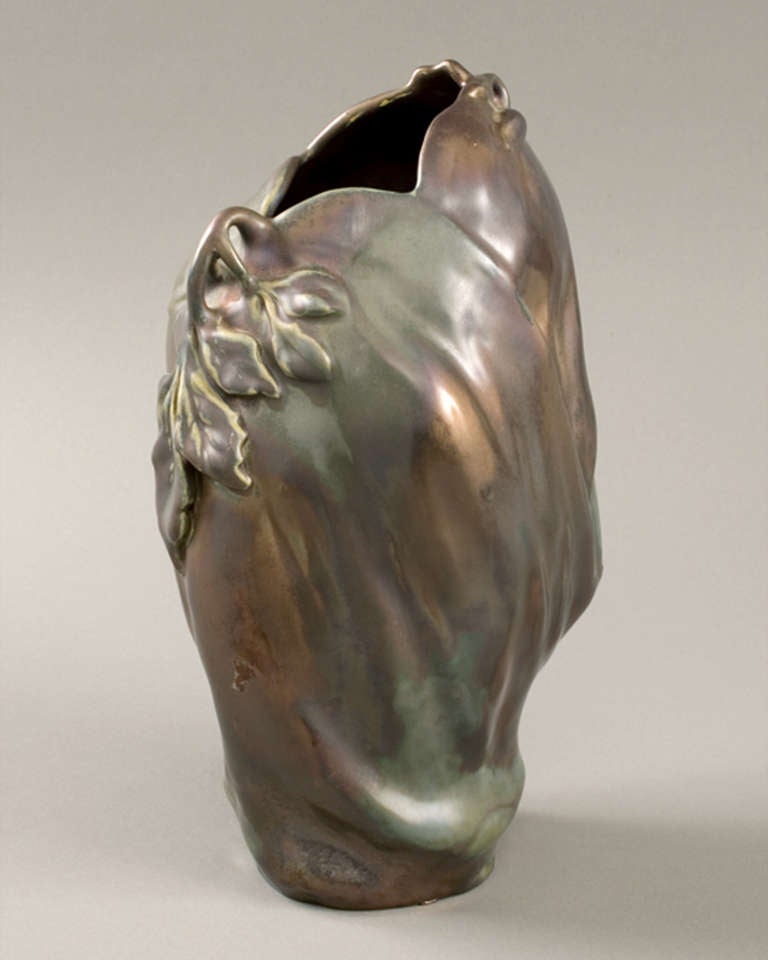 A French Art Nouveau “Eggplant” vase, by Keller and Guérin, following a design of Ernest Bussière, featuring iridescent gold, brown and green glazes.   The vase has gentle folds and is decorated with applied curving stems holding elongated leaves,