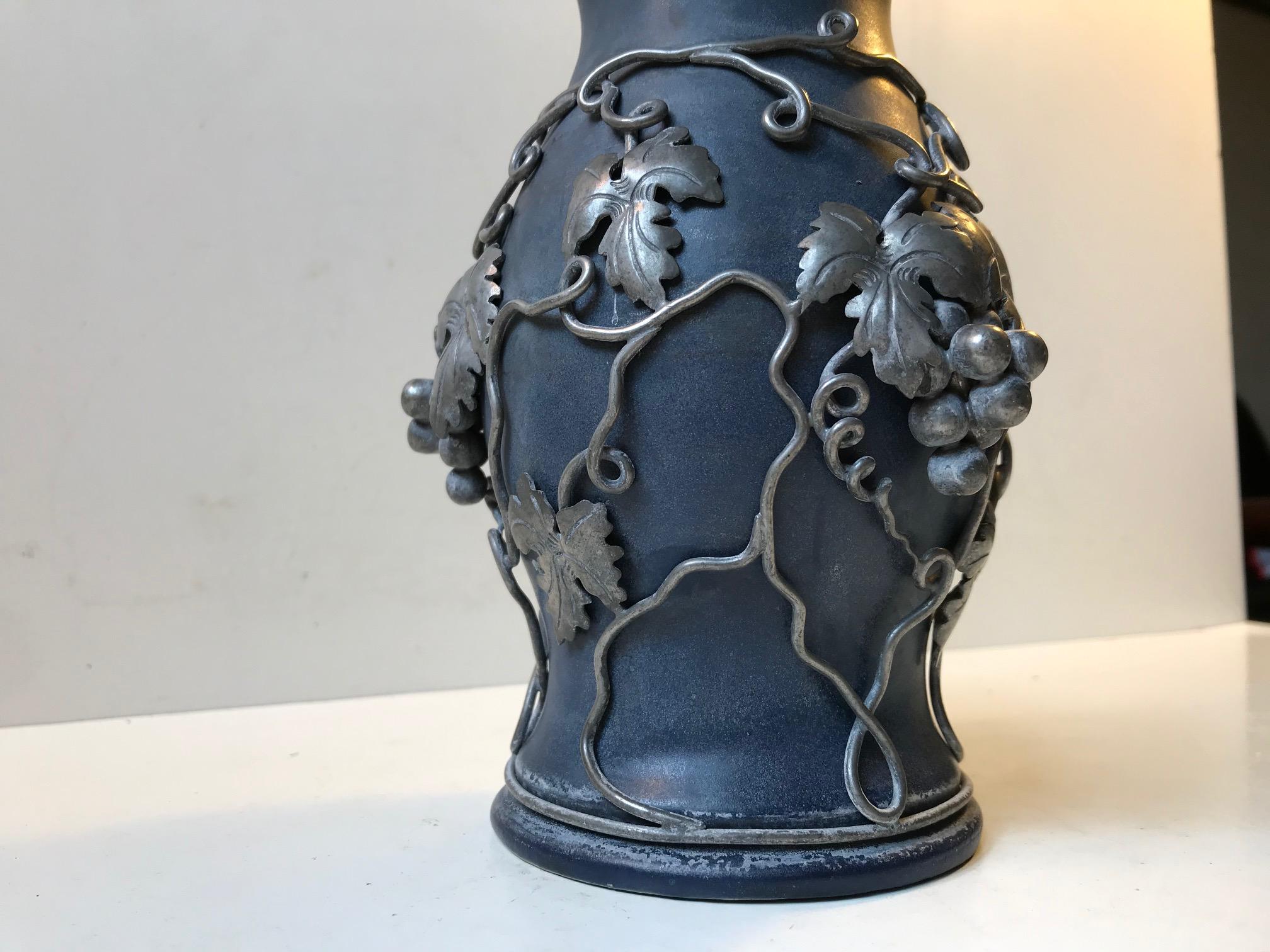 Art Nouveau vase with dark slightly matte 'blueberry' colored glaze and handmade grape ornamentation in pewter. Anonymous French ceramist circa 1900-1900s. It is signed indistinguishable.