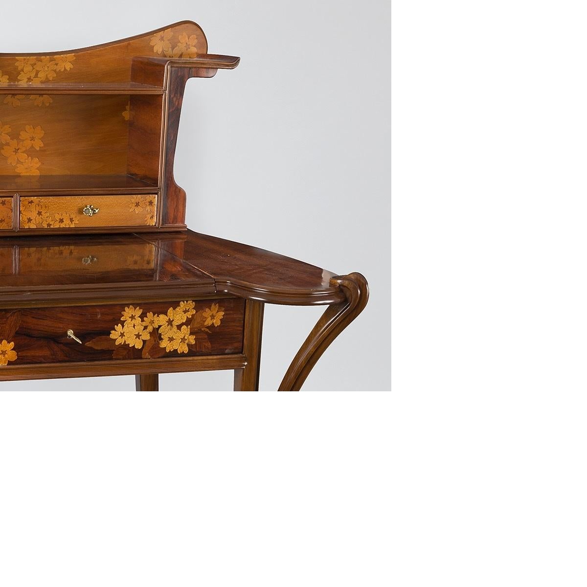 A French Art Nouveau desk in walnut, veneer wood fruit and bronze by Louis Majorelle. The three drawers of the desk are decorated in marquetry with flowers. The same pattern is repeated on the desk's upright piece, which features letter holders on