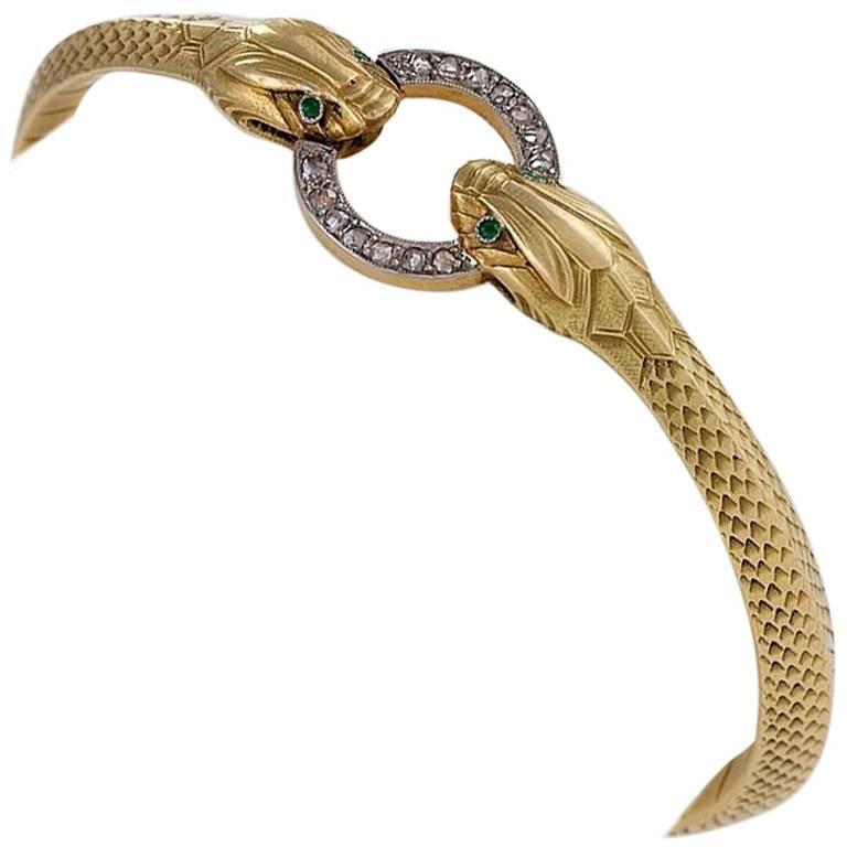 A French Art Nouveau 18 karat gold and platinum bangle bracelet with diamonds. The bangle bracelet has 14 rose-cut diamonds with an approximate total weight of .35 carat. The hinged bangle depicts a pair of facing serpents holding a platinum set
