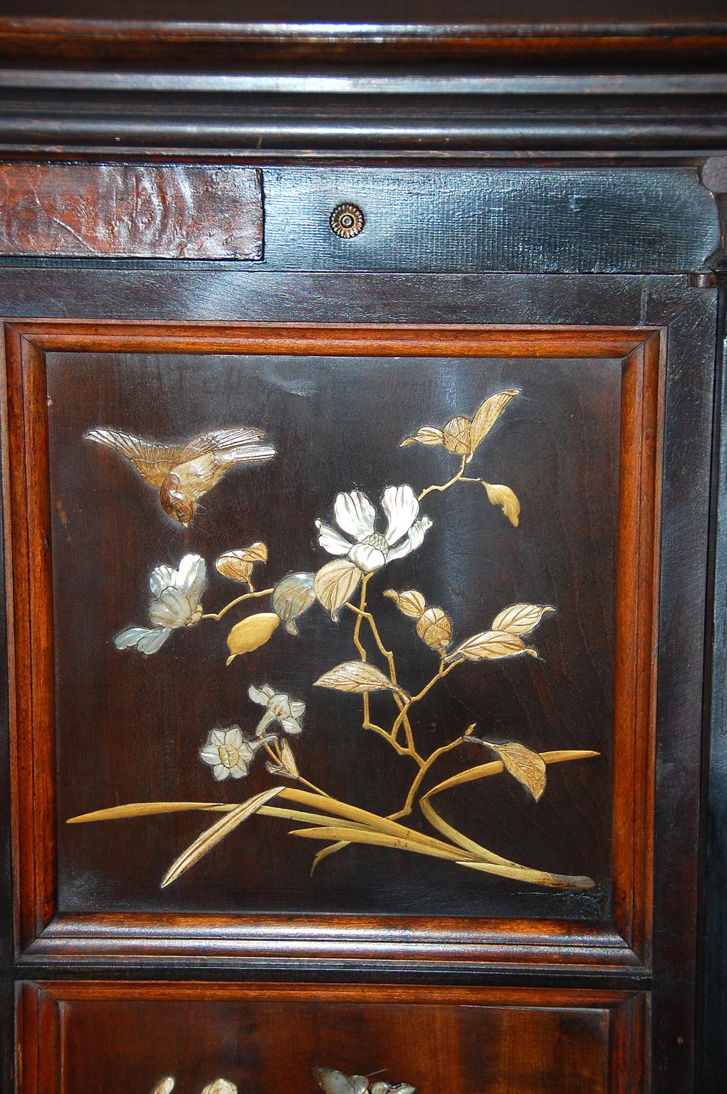 French Art Nouveau ebonized two door cabinet with double arched facade, lower shelf with mirrored back. Two cabinet doors with four inlaid and overlaid naturalistic panels of birds, butterflies and flowers in mother of pearl and bone. The carcass of