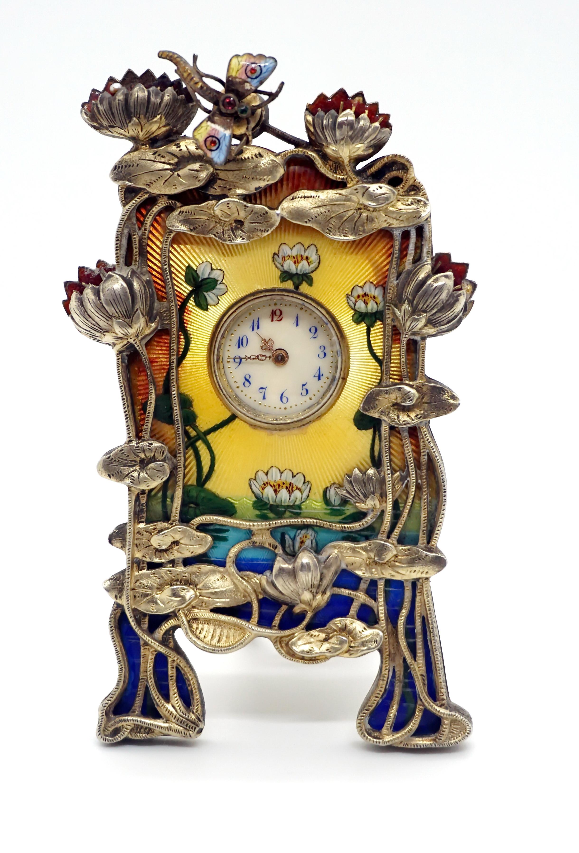 Exquisite French enamel table clock from the period circa 1900

Metal case and movement partly gouilloché. Enamel painting on the front - waters with water-lilies against a sunny yellow background. Above it, sculptured water-lily plants made from